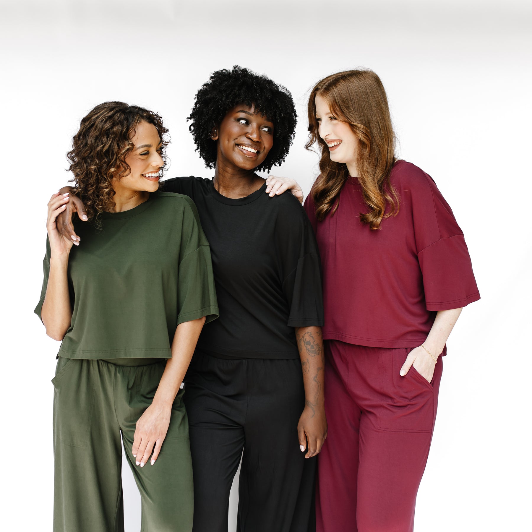 Three female models standing side by side wearing the Women's Short Sleeve Tee in Fir, Midnight and Burgundy with matching wide leg pants