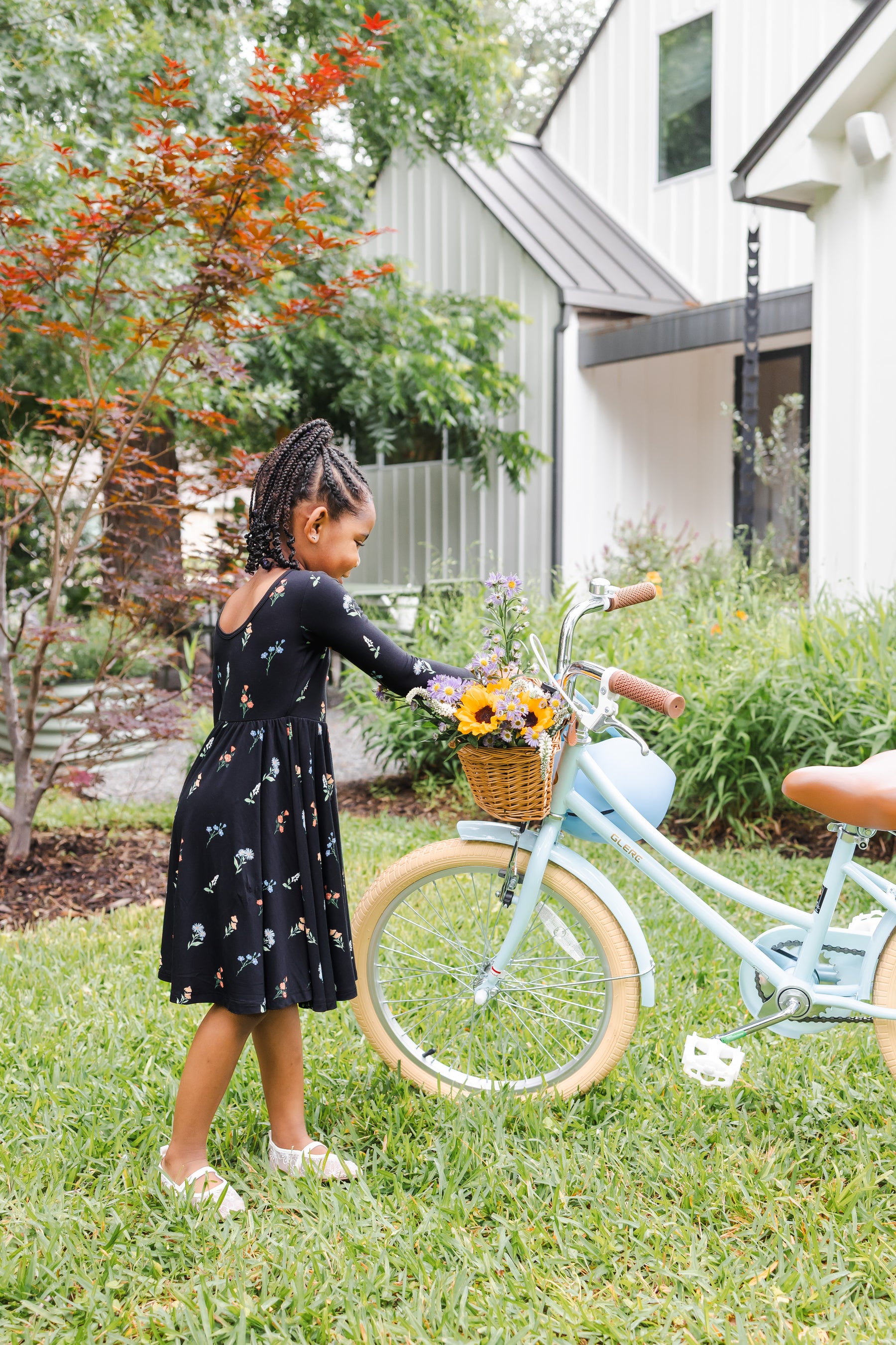 Girl playing outdoors with a bicycle in a garden wearing Long Sleeve Twirl Dress in Midnight Wildflower print