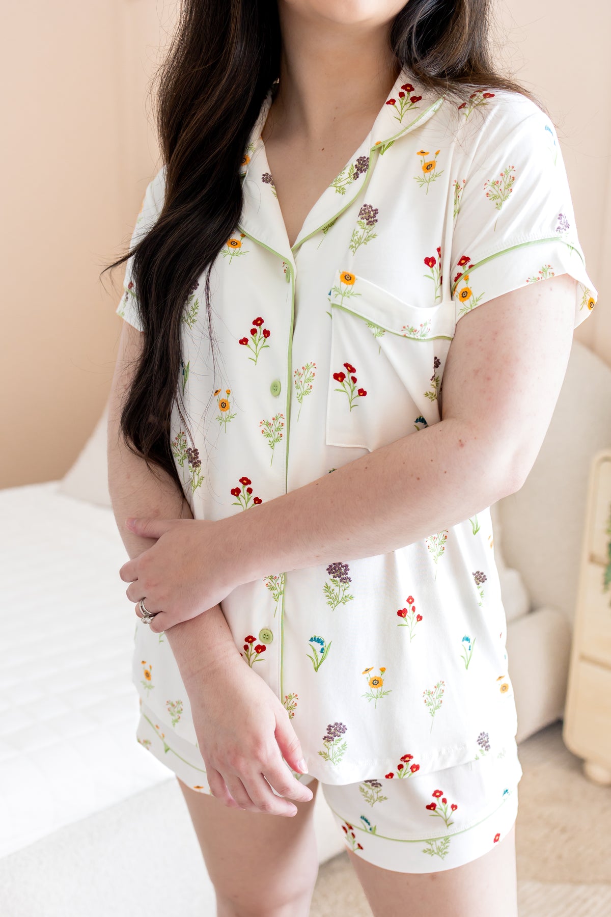 Woman wearing a white pajama set with floral patterns in a bedroom setting.