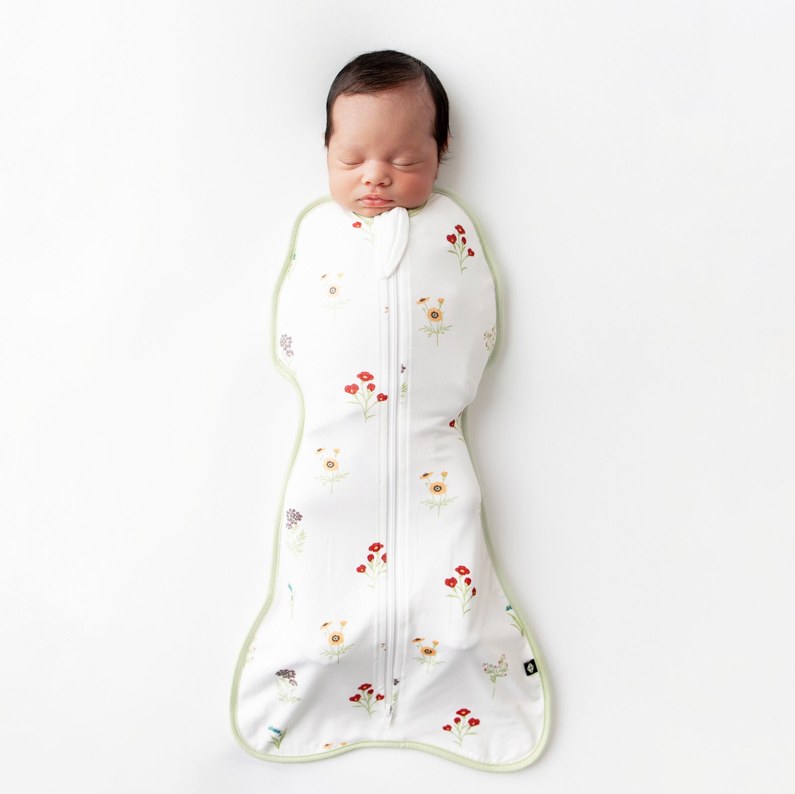 Sleeping newborn laying on a light neutral surface wearing the Swaddle Bag in Wildflower 0.5