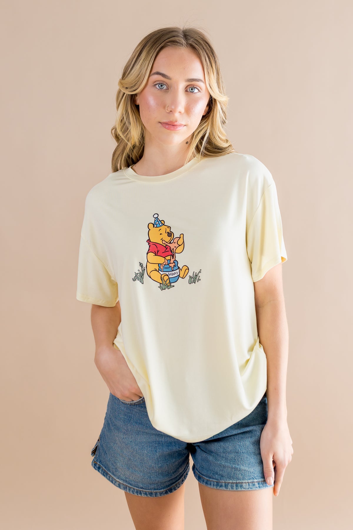 Female modeling the Women's Graphic Tee in Winnie the Pooh on Chamomile paired with medium wash jean shorts