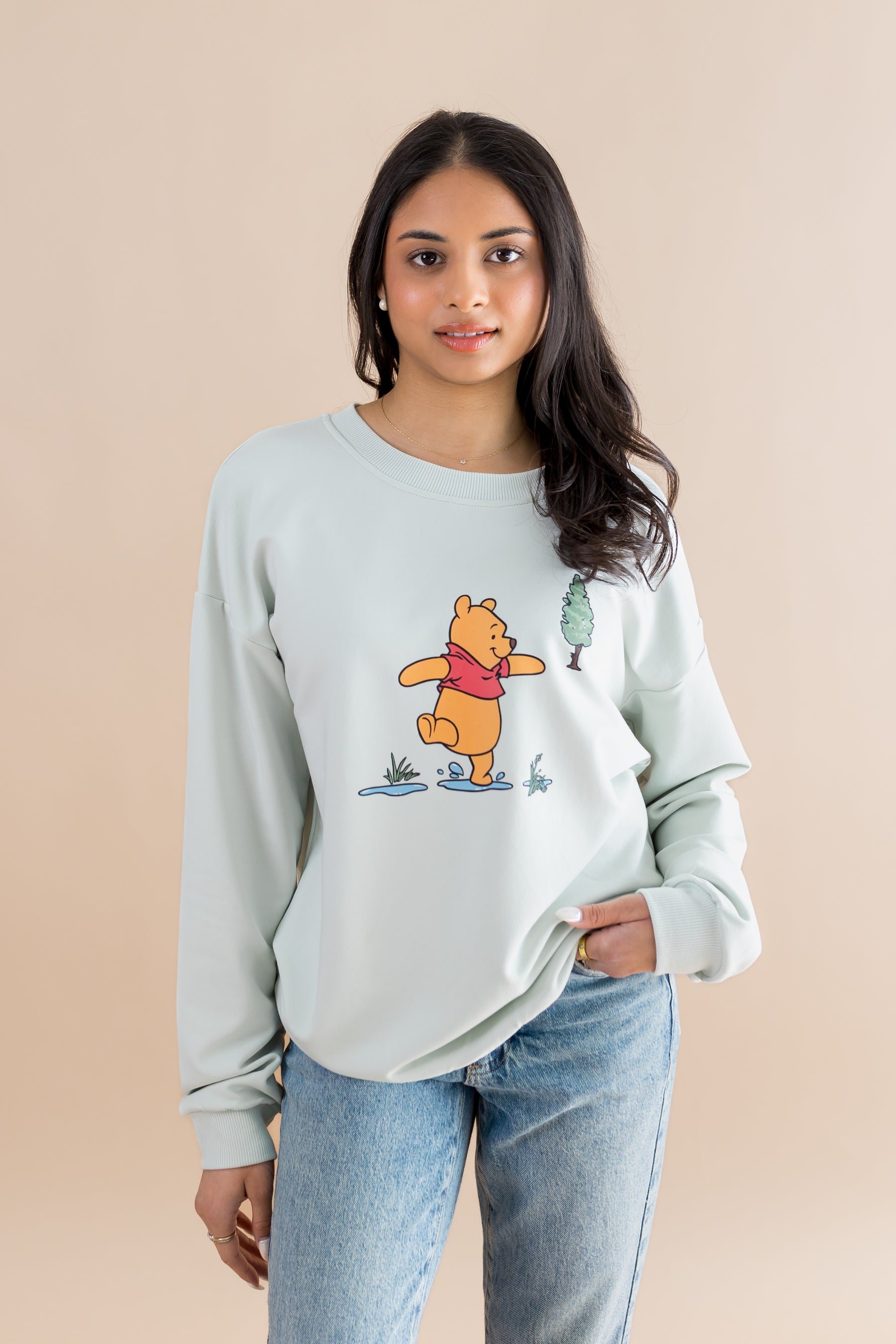 Female modeling the Women's Sweatshirt in Winnie the Pooh on Dew paired with light wash jeans