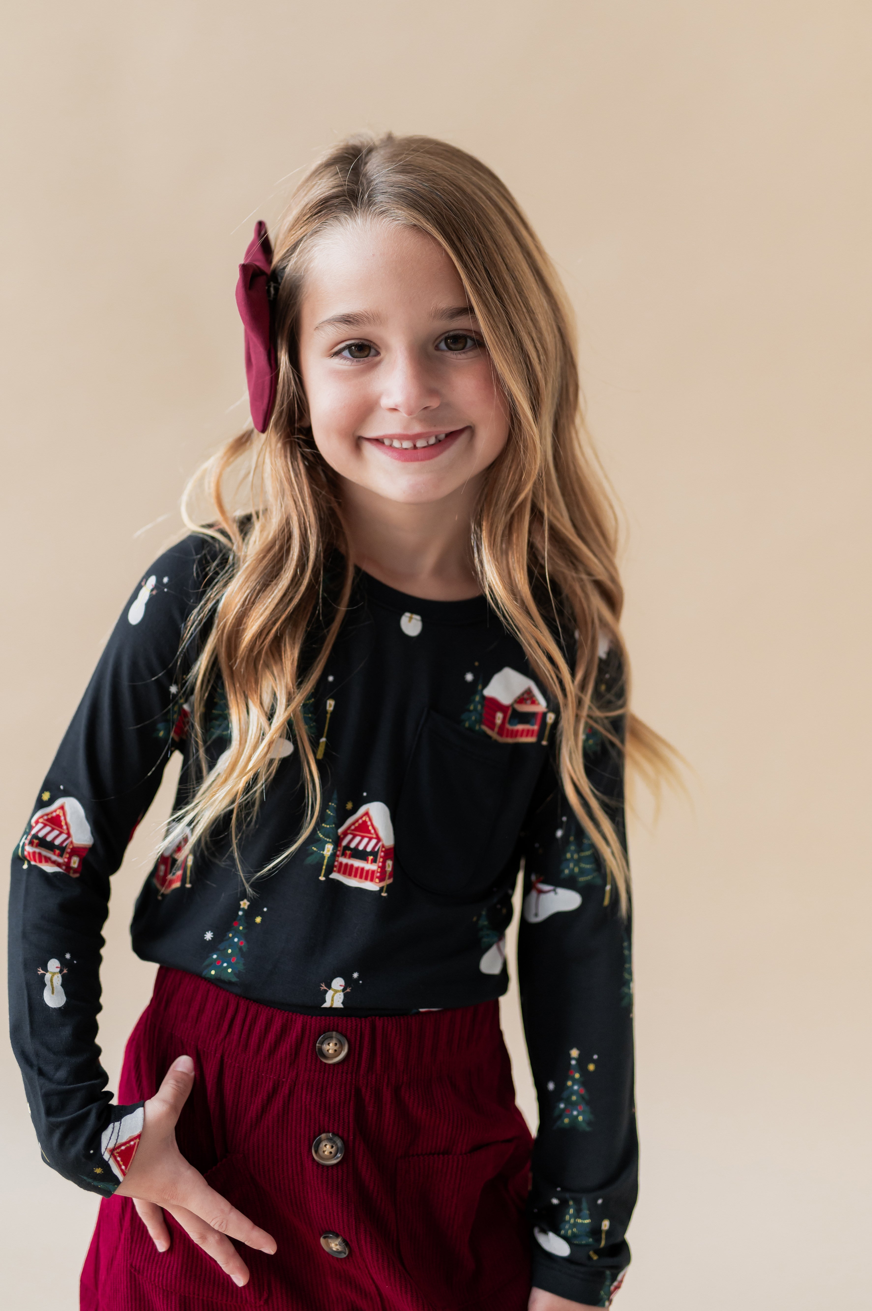 Girl posing in medium alligator clip bow in burgundy color over holiday print t-shirt and burgundy color skirt on a beige background
