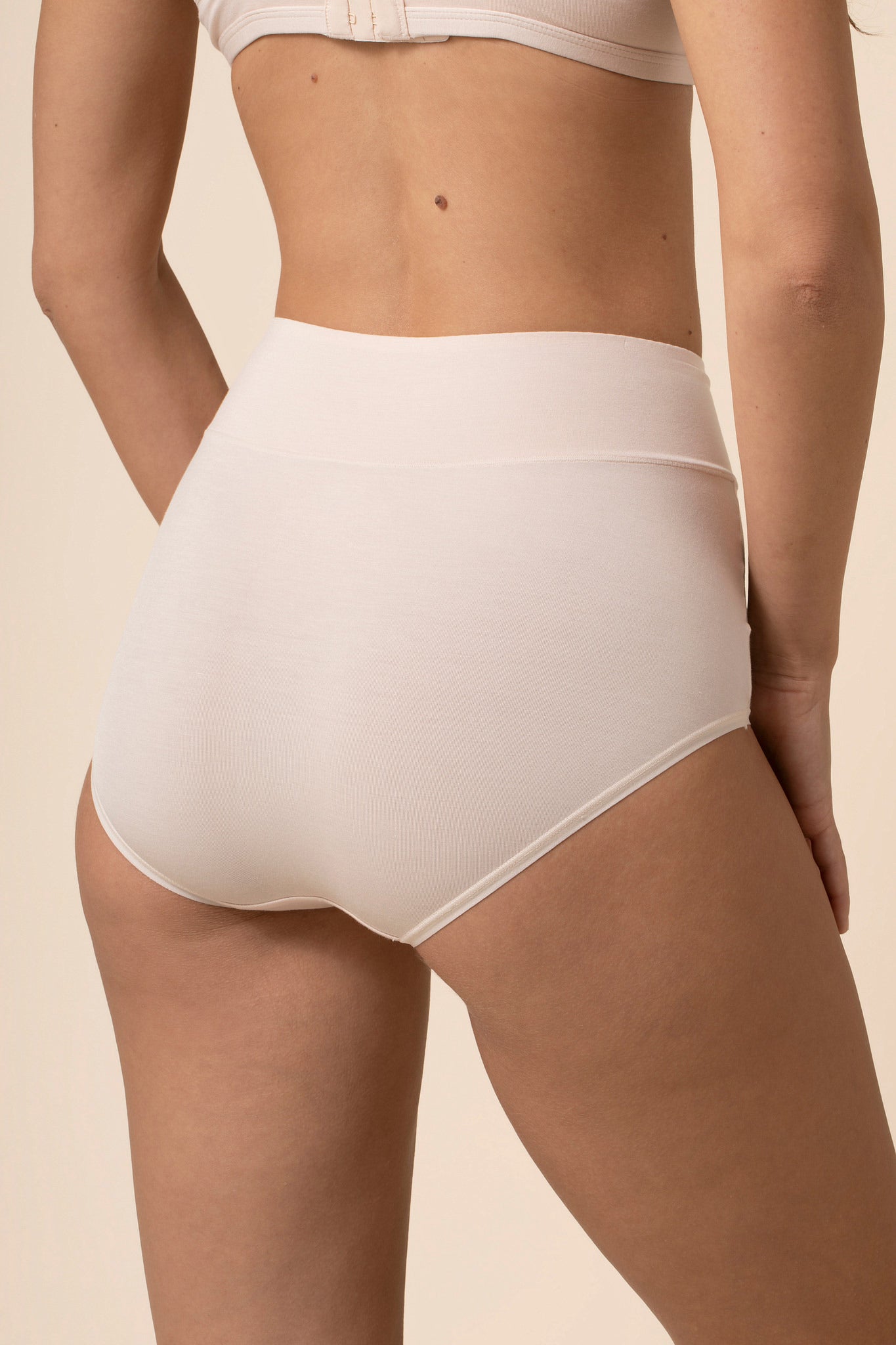 Person wearing off white high-waisted underwear on a beige background