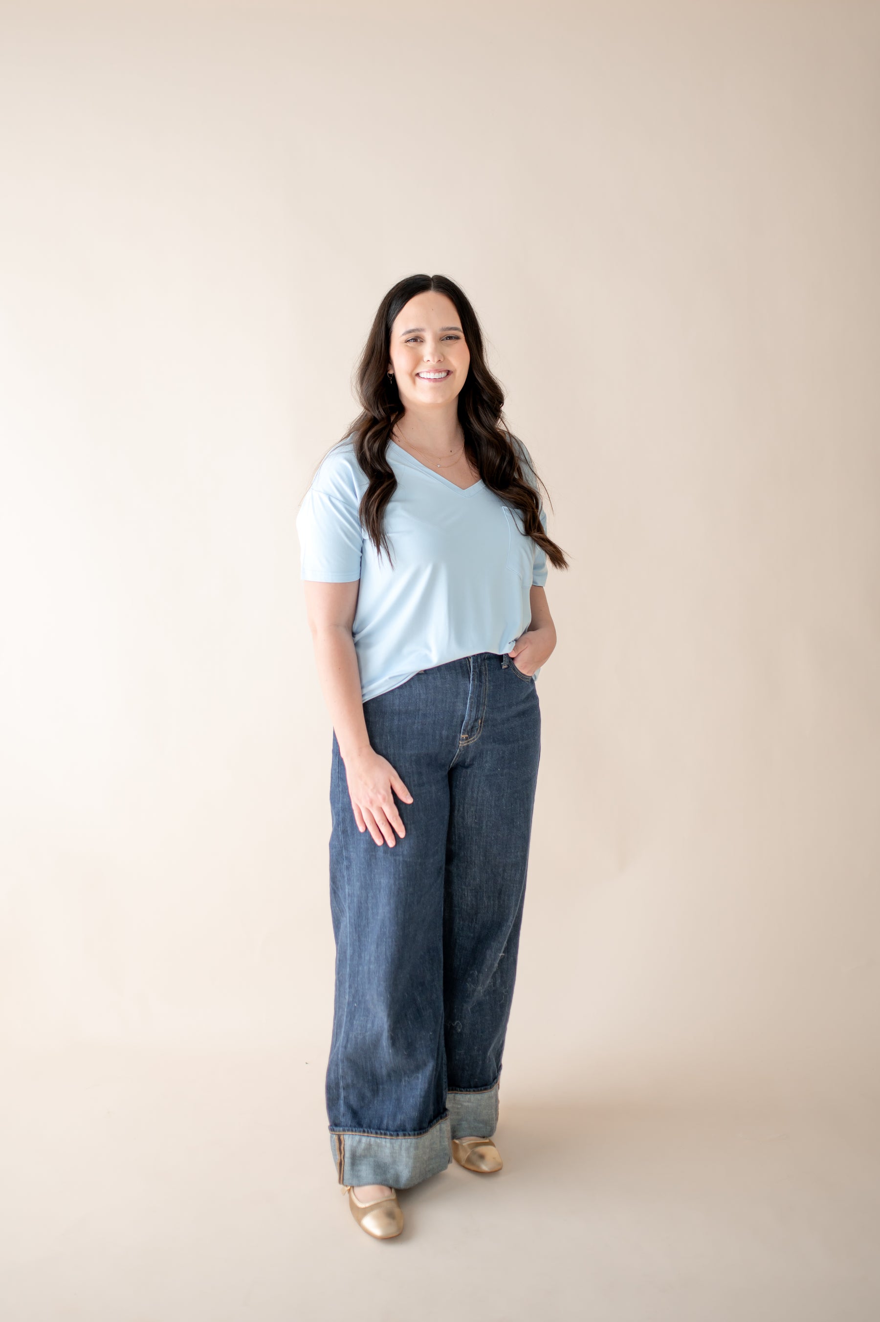 Smiling female modeling the Women's Relaxed Fit V-Neck in Breeze paired with medium wash jeans in front of a light neutral background