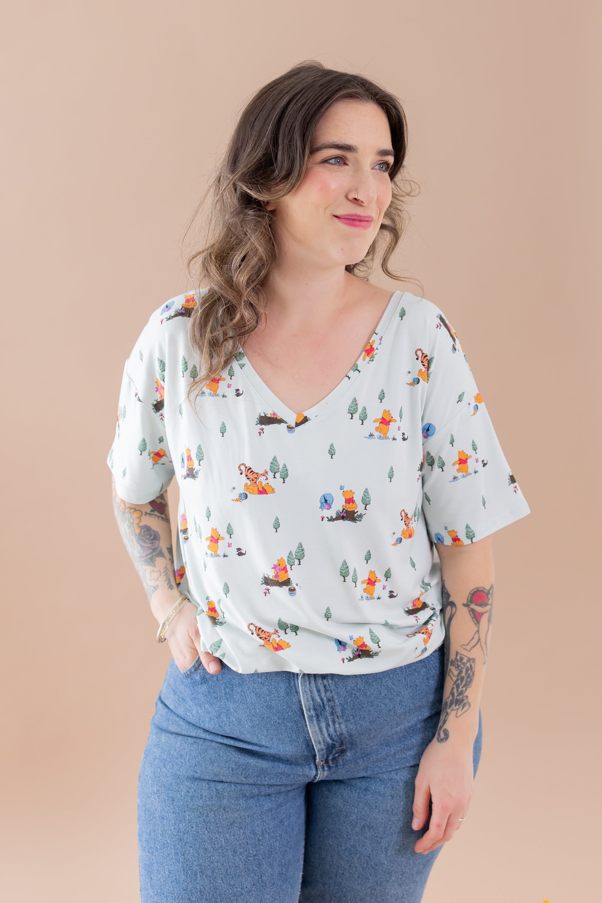 Female modeling the  Women's Relaxed Fit V-Neck in Winnie the Pooh Hundred Acre Wood paired with medium wash jeans