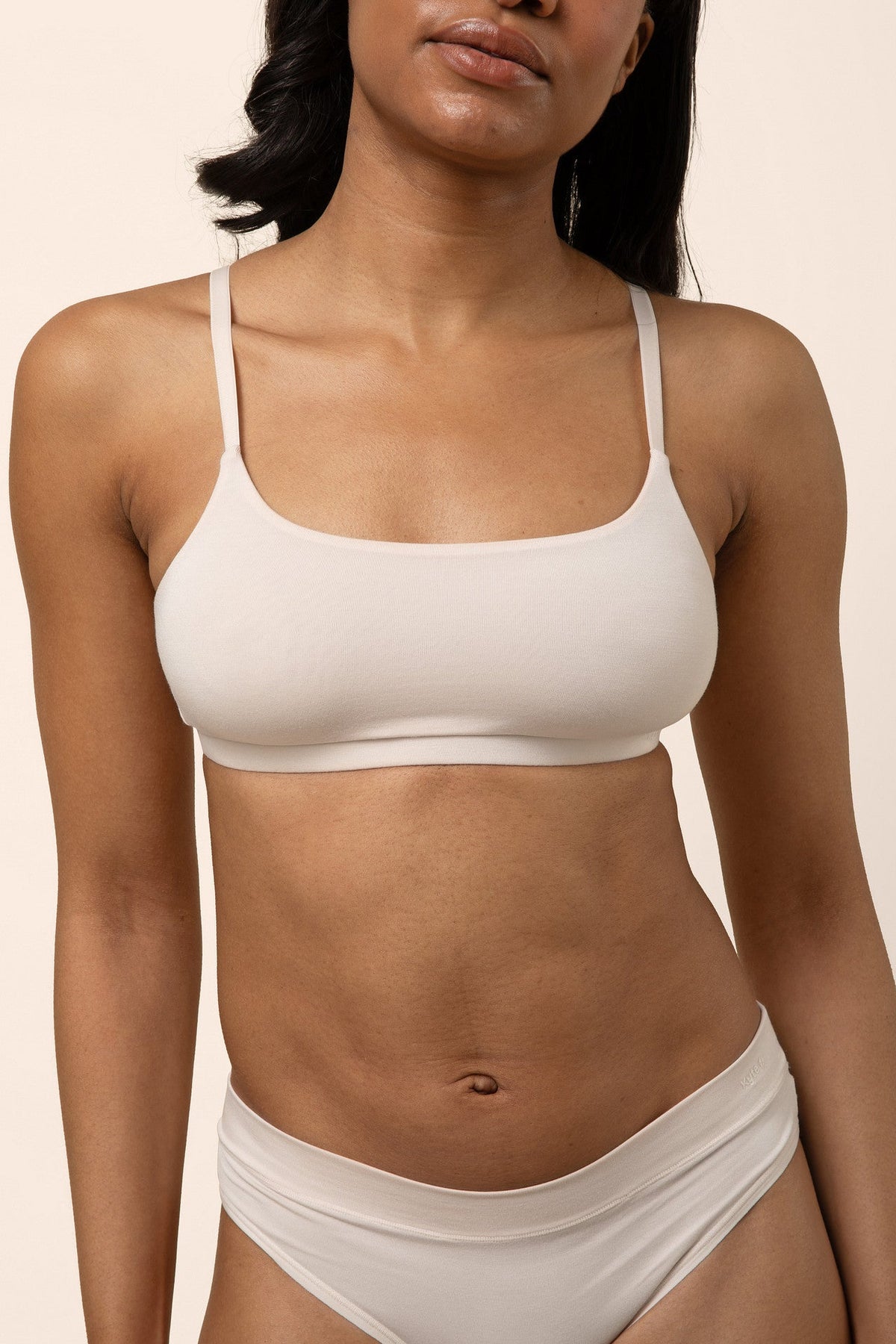 Woman wearing a light beige bra and underwear set against a beige background
