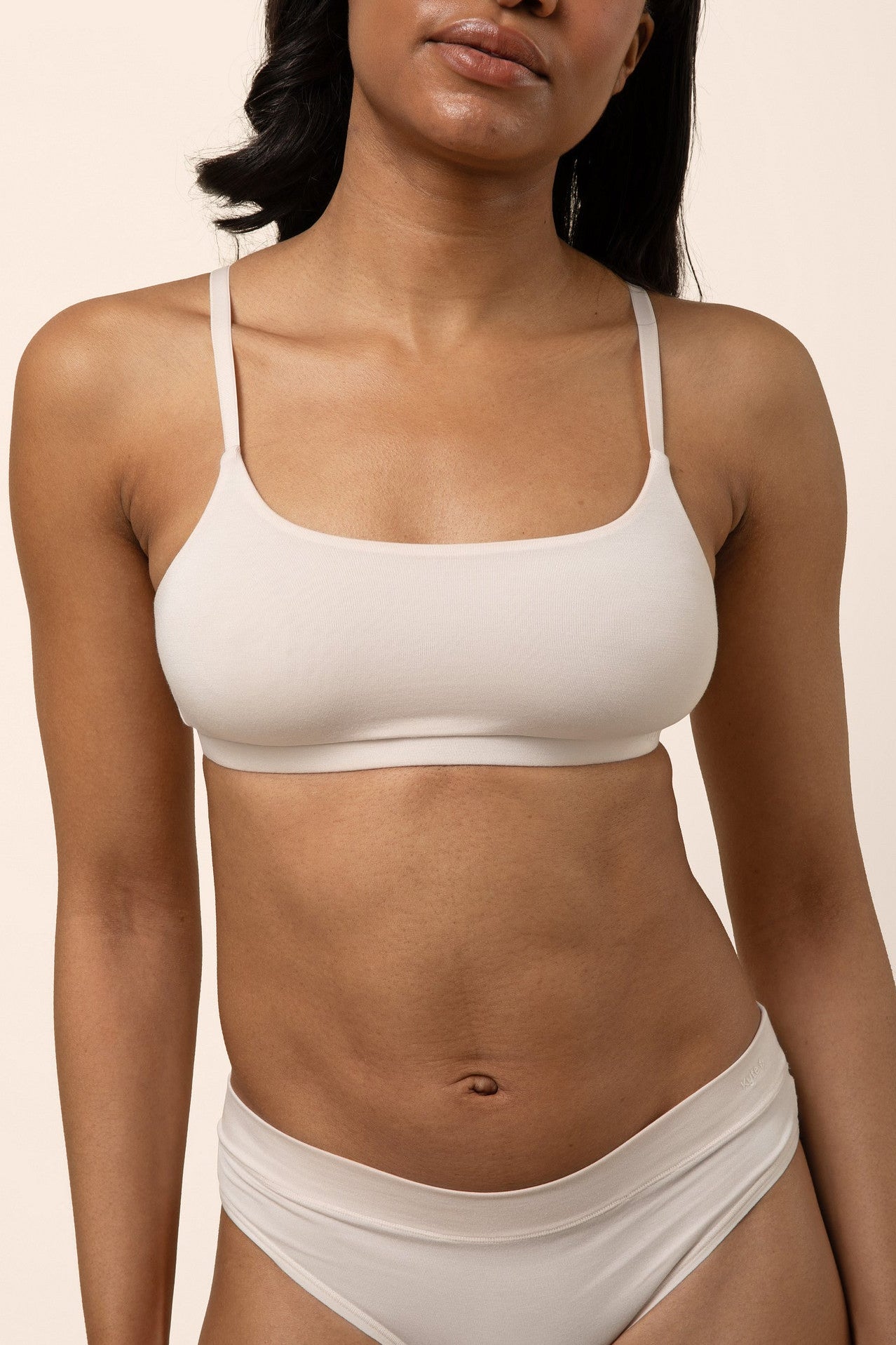 Woman wearing a light beige bra and underwear set against a beige background