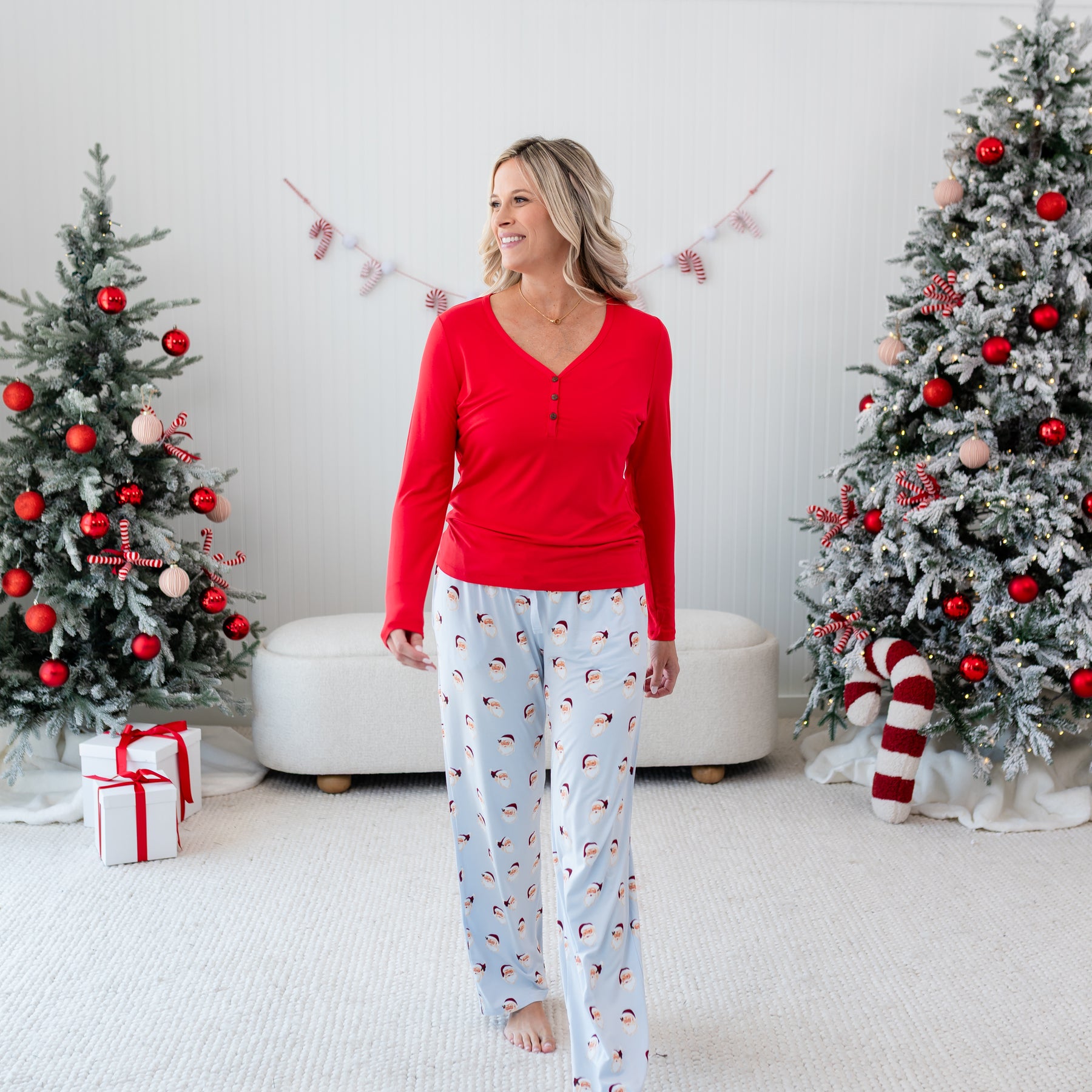 Female walking in front of a Christmas themed back drop wearing the Women's Long Sleeve Henley Tee in Cardinal with Vintage Santa Lounge Pants