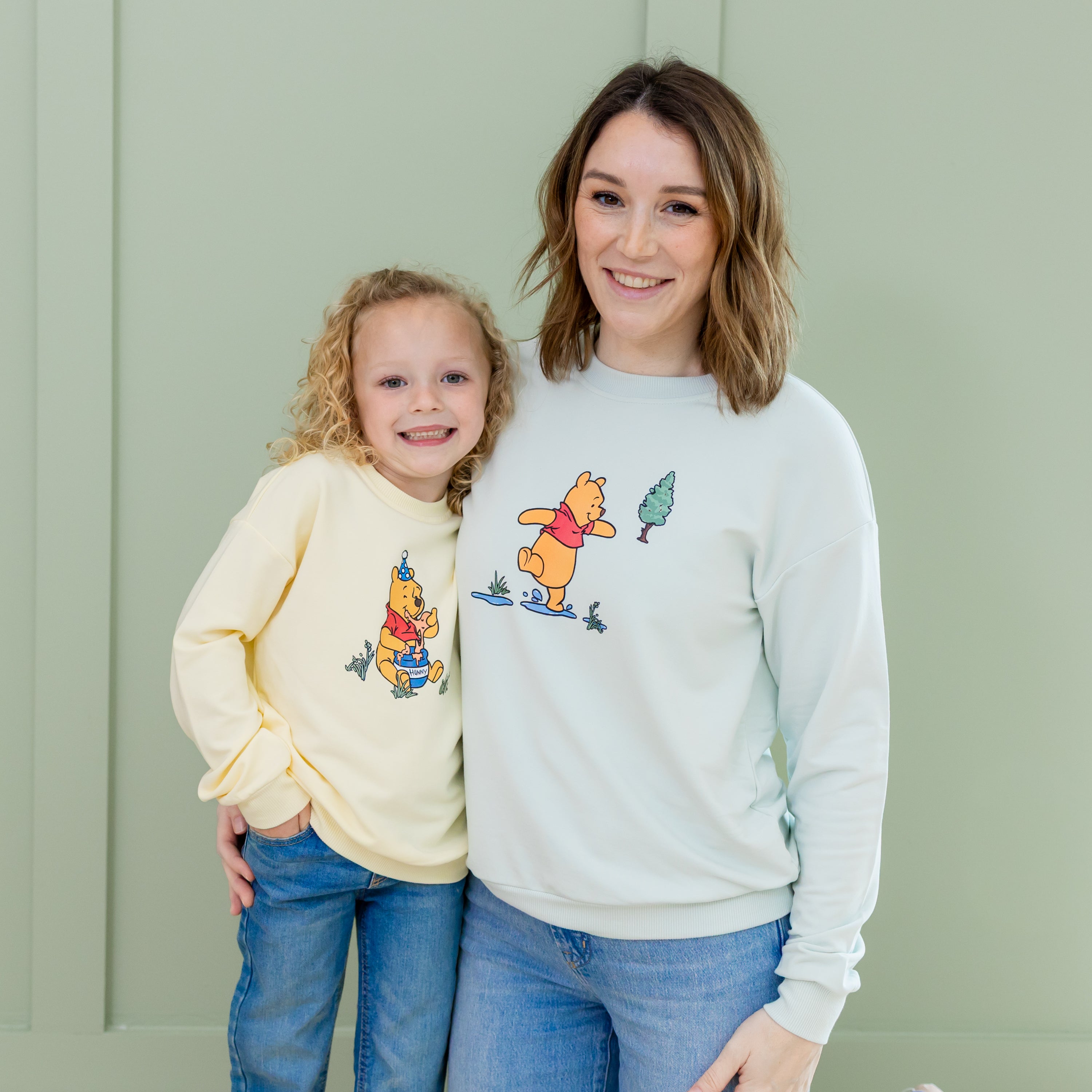 Mother and young daughter standing side by side in Winnie the pooh chamomile and Winnie the pooh dew sweatshirts