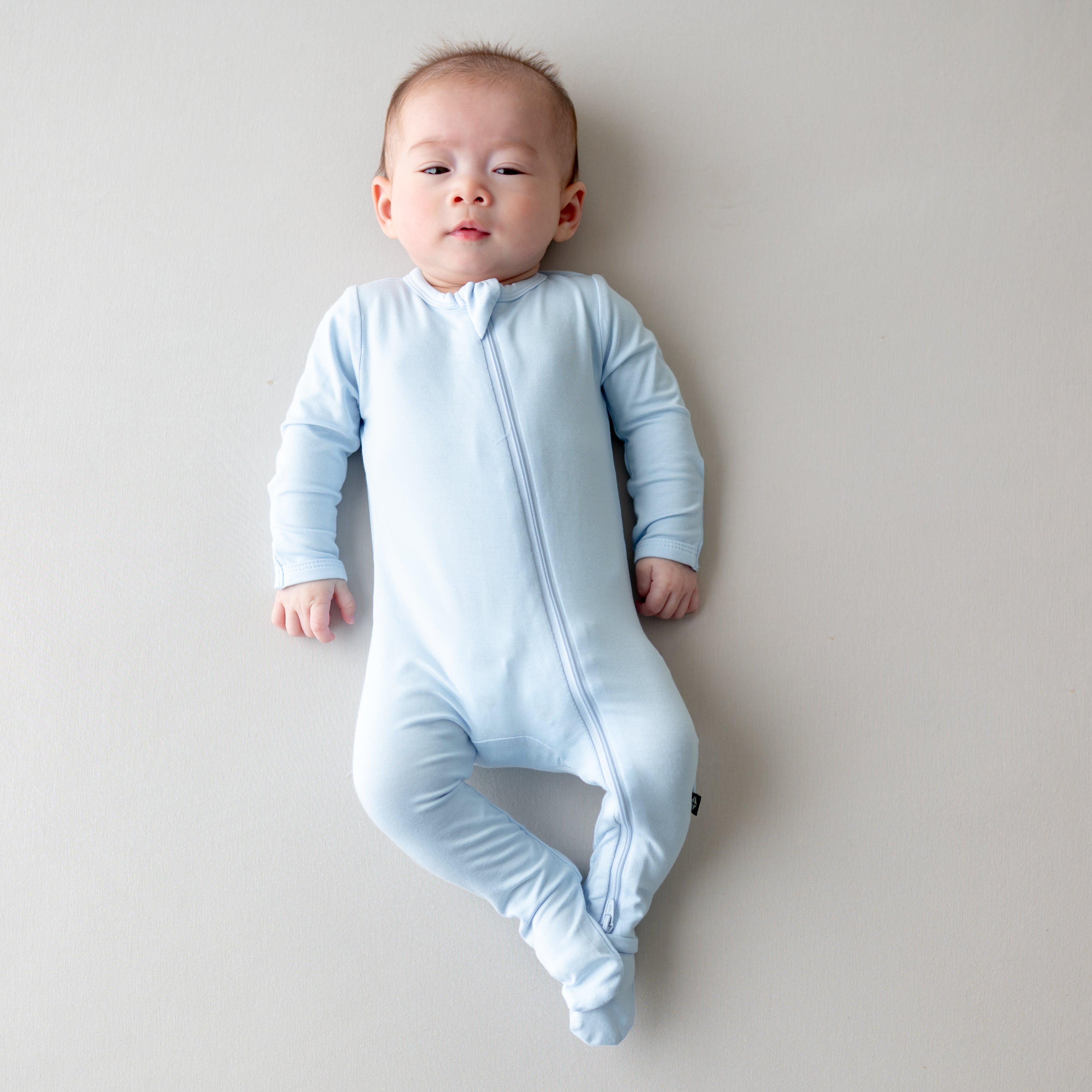 Baby wearing a light blue zippered footie on a plain background