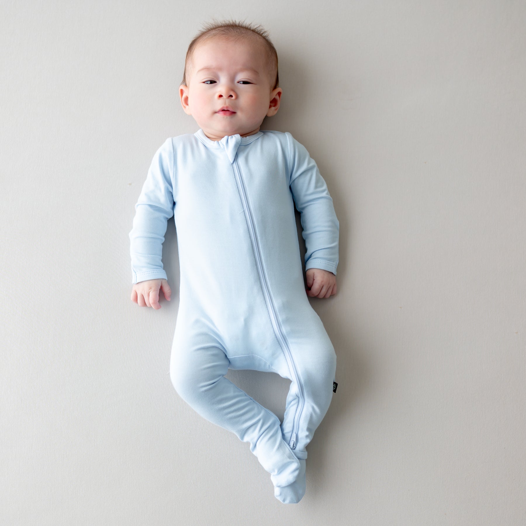 Baby wearing a light blue zippered footie on a plain background
