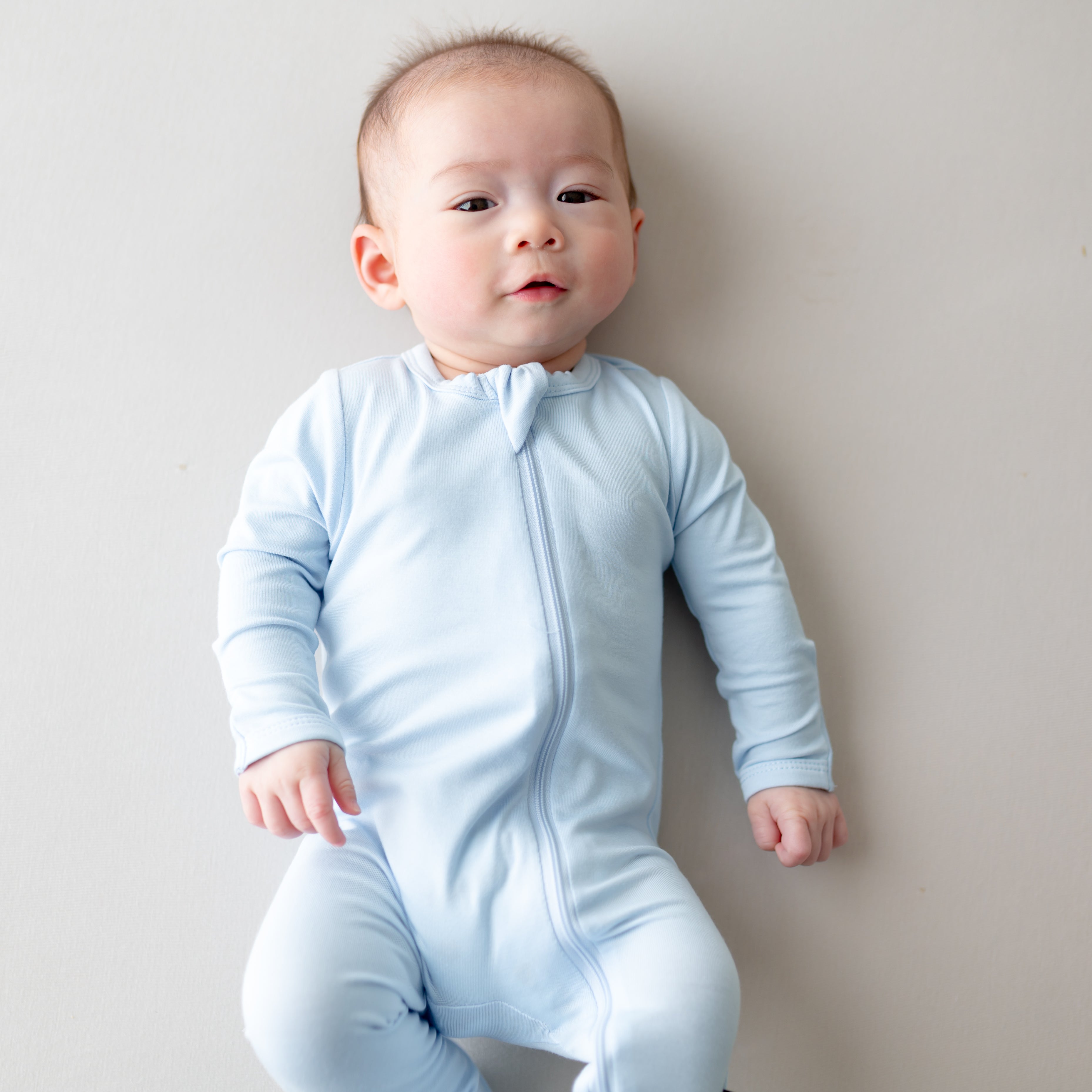 Baby wearing a light blue zippered footie against a plain background