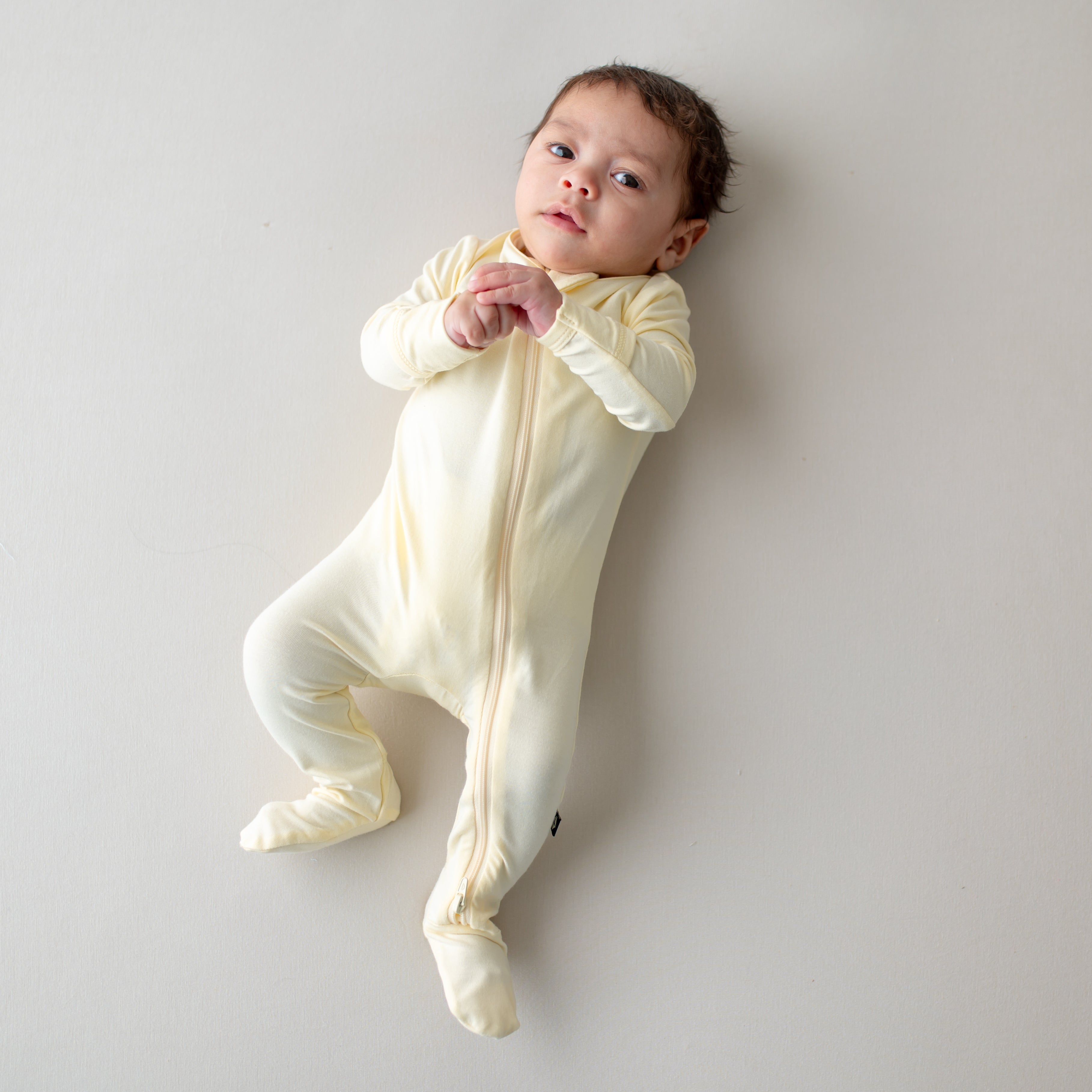 Baby in a yellow-colored zippered footie lying on a light gray background