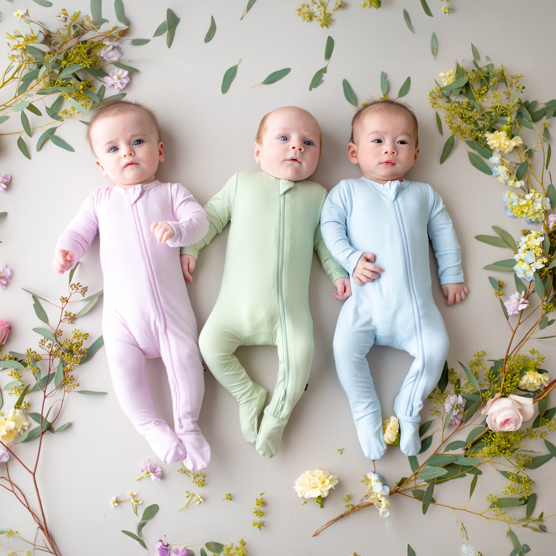 Three babies in colorful zippered footies lying on a floral background