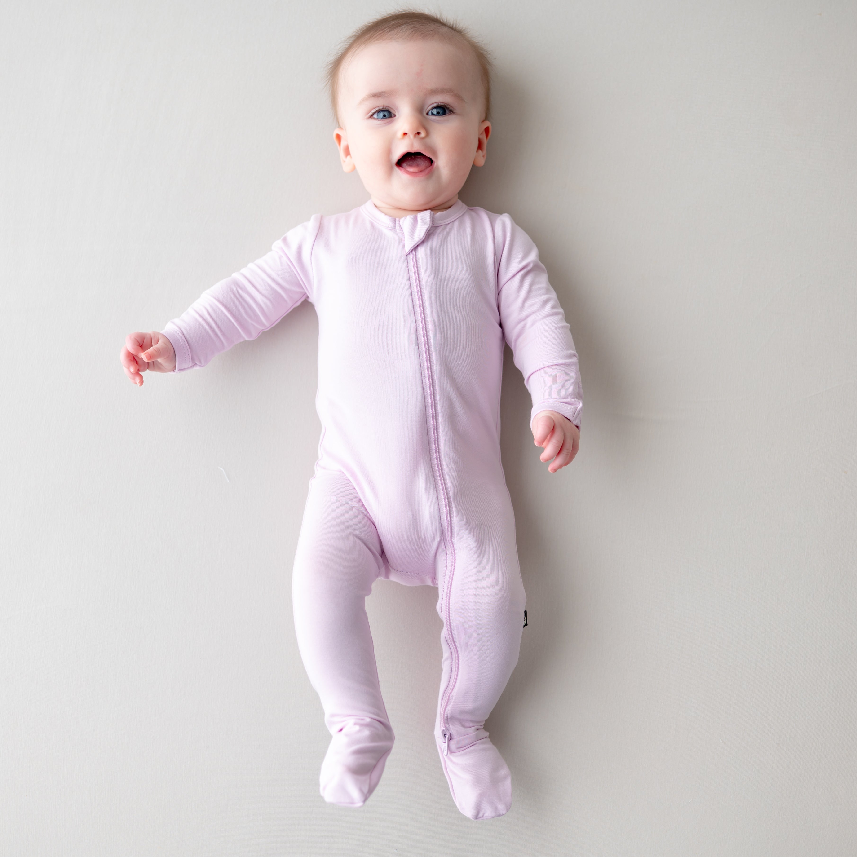 Baby wearing a light purple zippered footie on a plain background