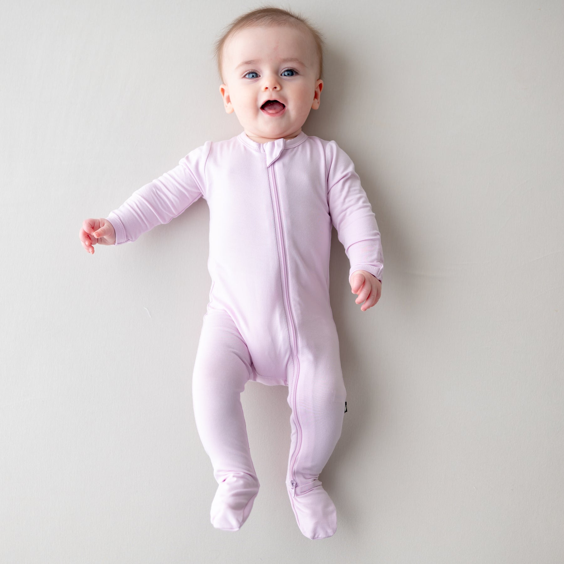 Baby wearing a light purple zippered footie on a plain background