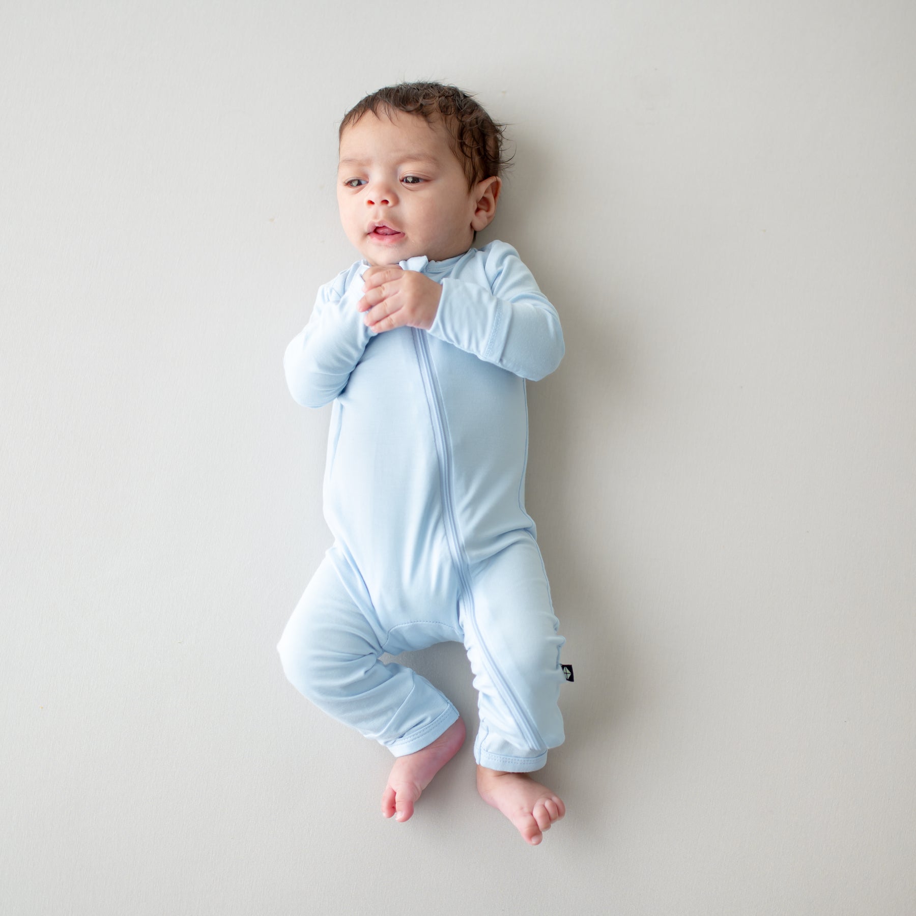 Baby wearing a light blue zippered romper on a plain background