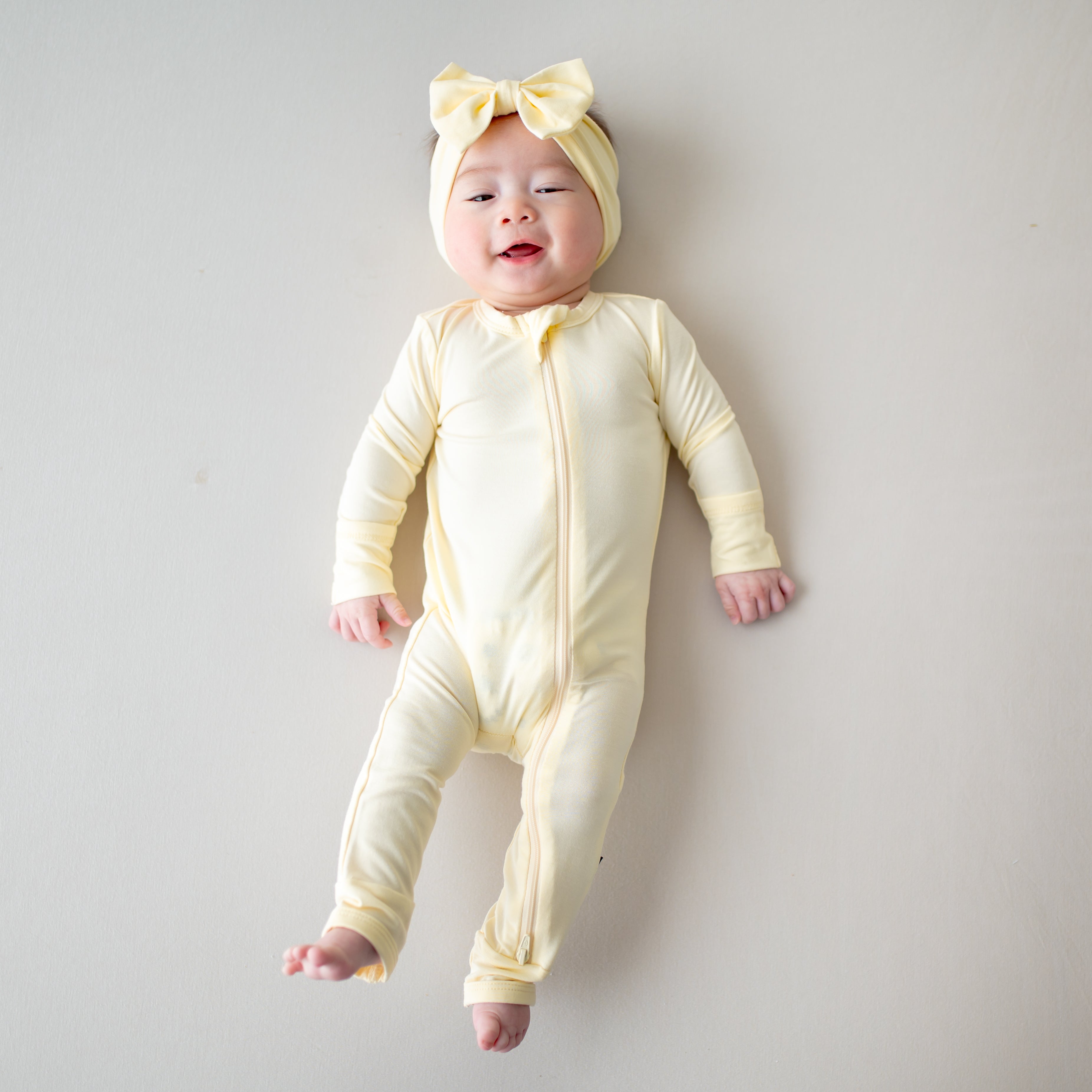 Baby wearing a light yellow zippered romper with a matching bow