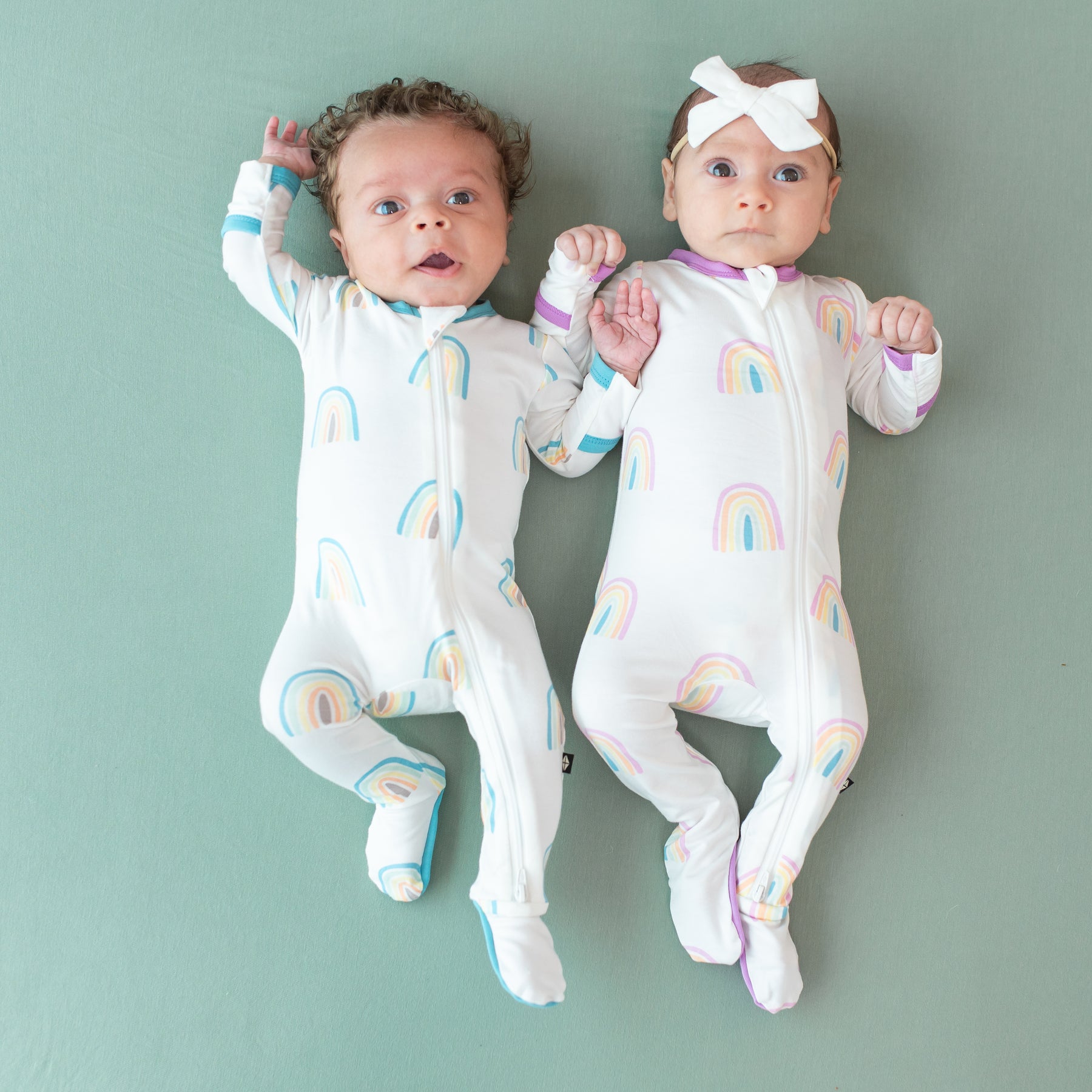 Two babies wearing Zippered Footies in Poi and Makai Rainbow