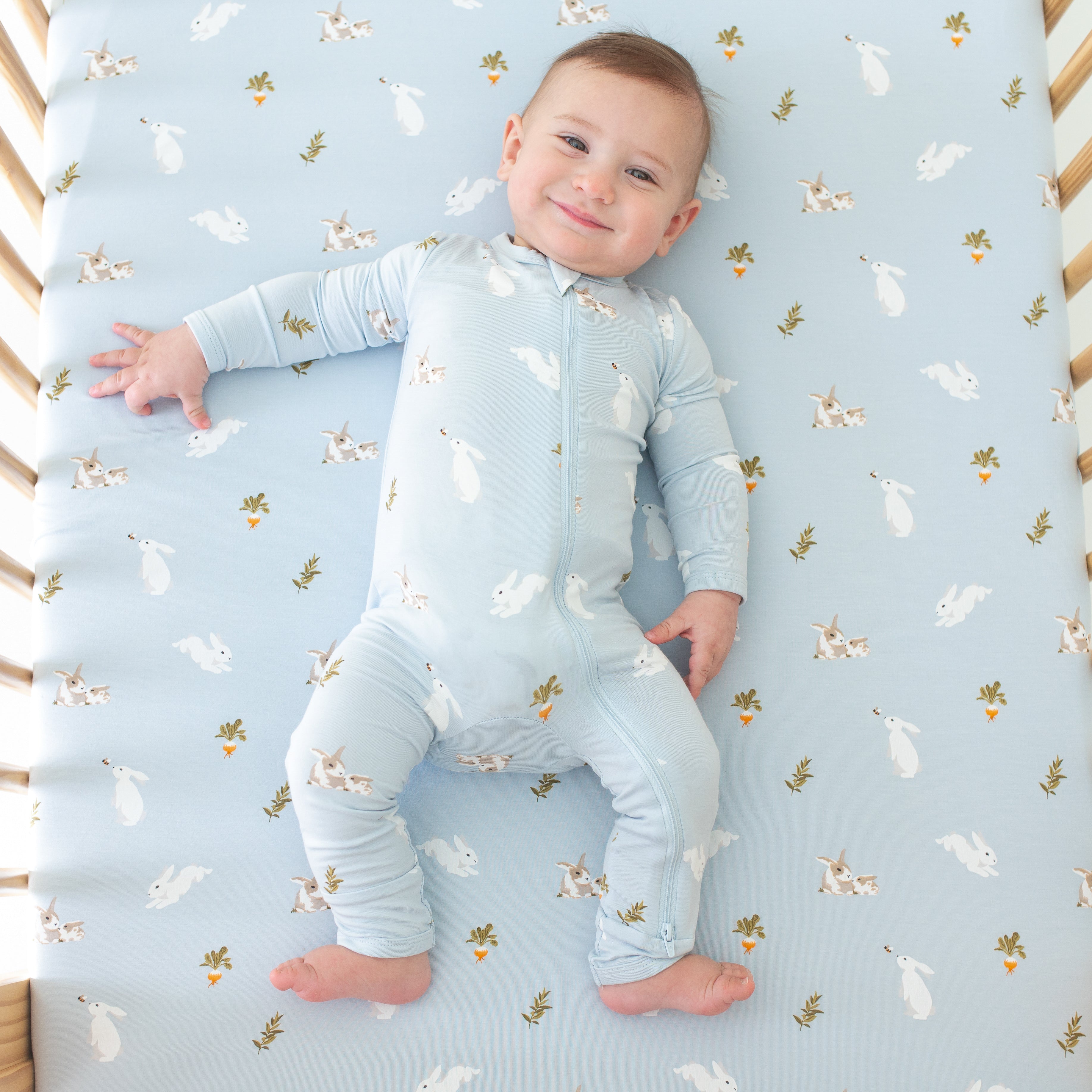 Baby smiling wearing Zippered Romper in Ice Rabbit in a Ice Rabbit crib sheet