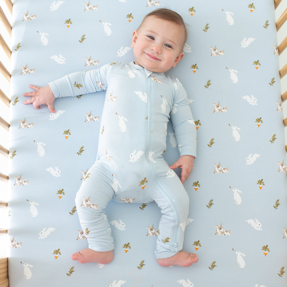 Baby smiling wearing Zippered Romper in Ice Rabbit in a Ice Rabbit crib sheet