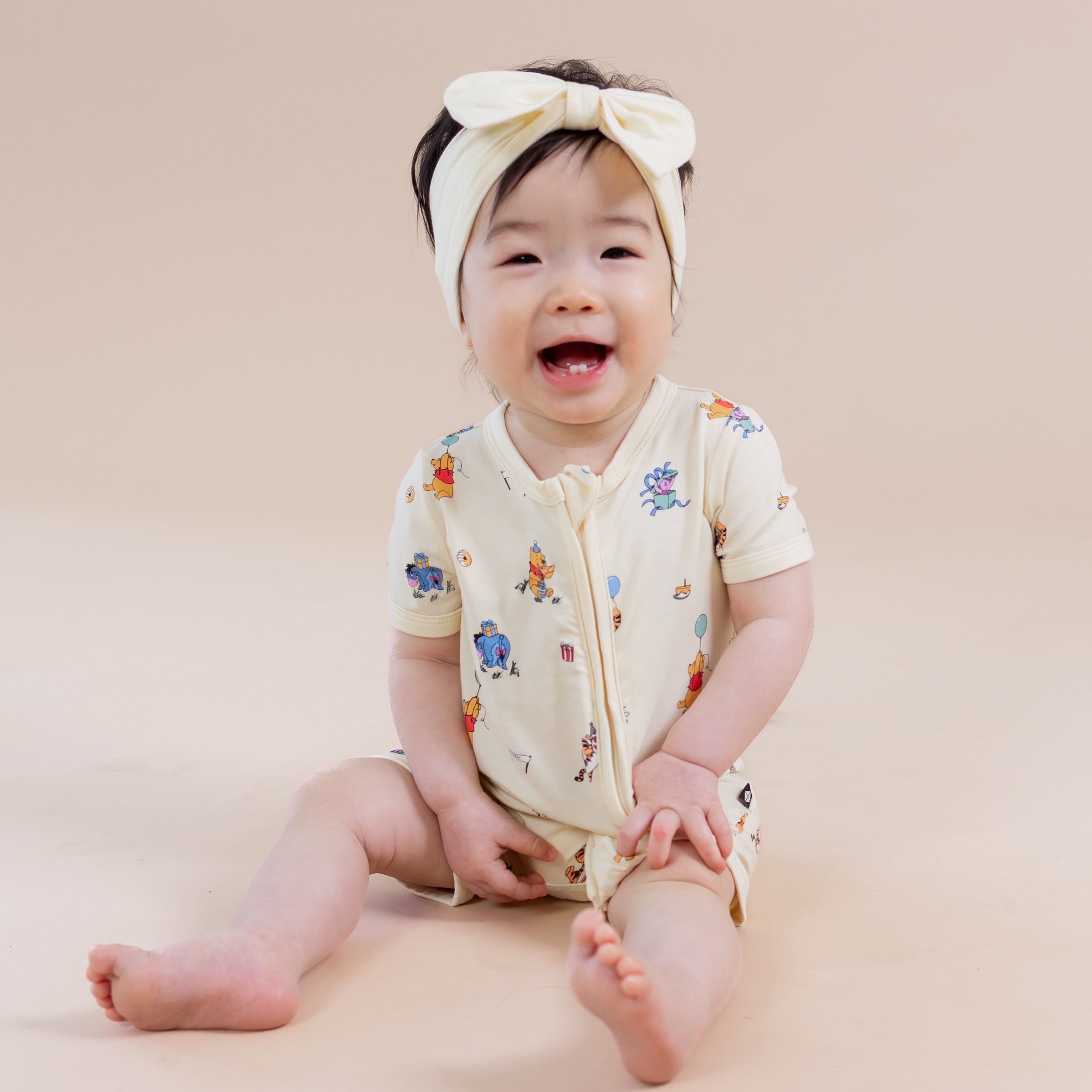 Young smiling girl sitting wearing the Zipper Shortall Romper in Winnie the Pooh Celebration