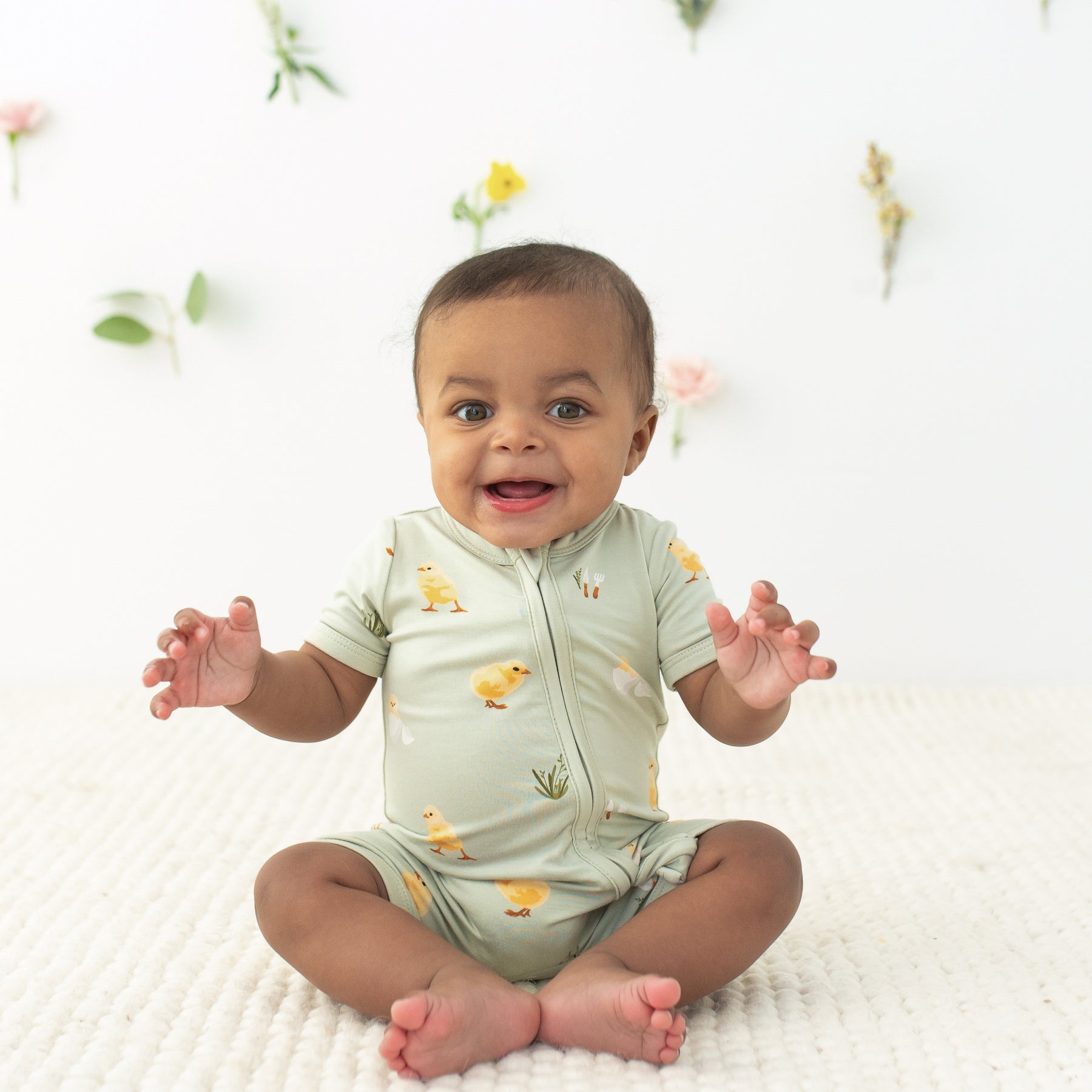 Baby sitting wearing Zipper Shortall Romper in Aloe Chick