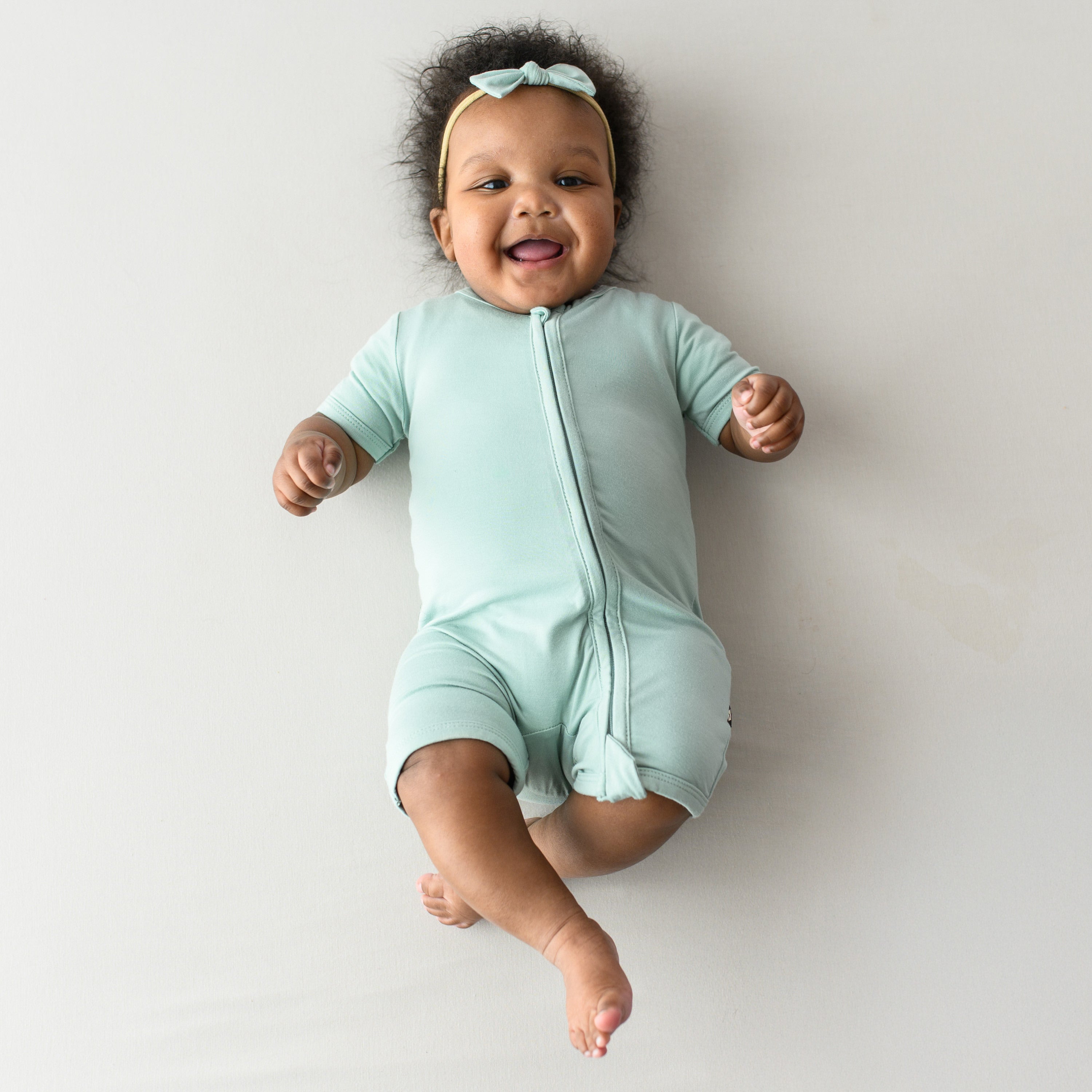 Smiling baby modeling Zipper Shortall Romper in Sage with matching bow