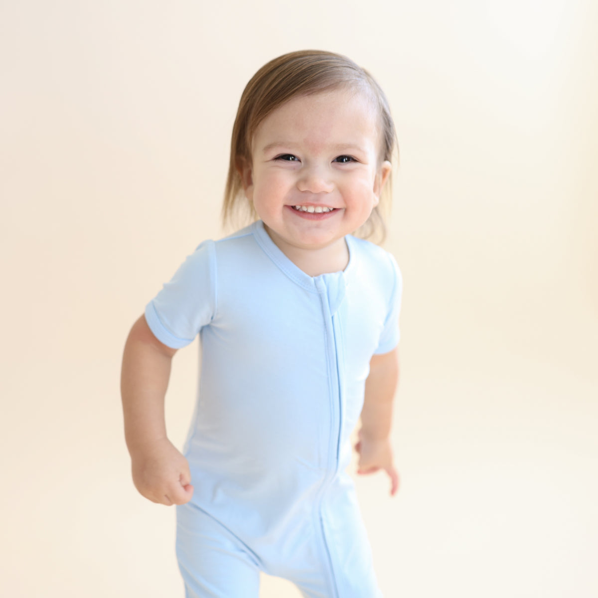 Young smiling boy wearing the Zipper Shortall Romper in Breeze