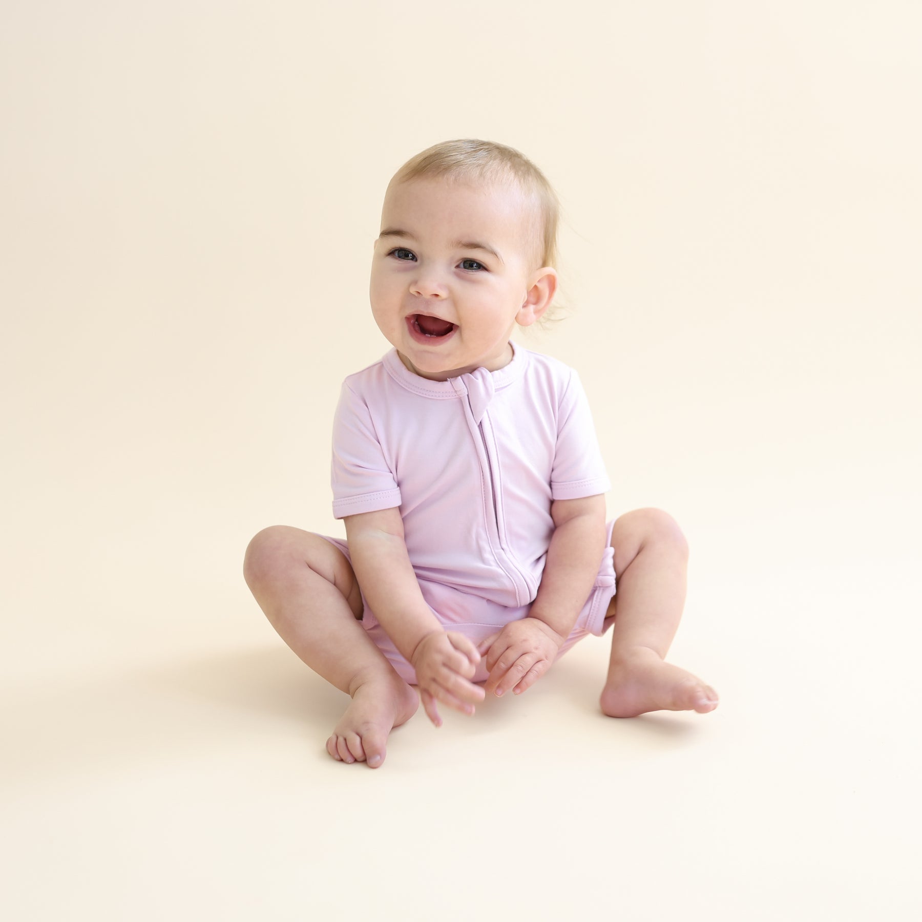 Young toddler sitting on the floor wearing the Zipper Shortall Romper in Thistle