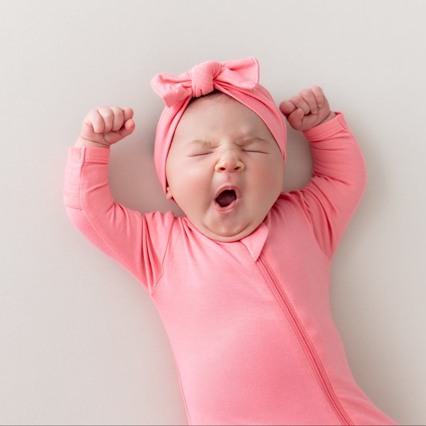 baby yawning wearing zippered footie and bow in guava
