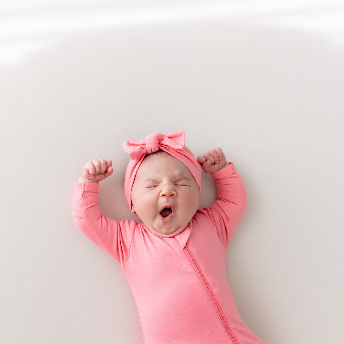 baby yawning wearing zippered footie and bow in guava