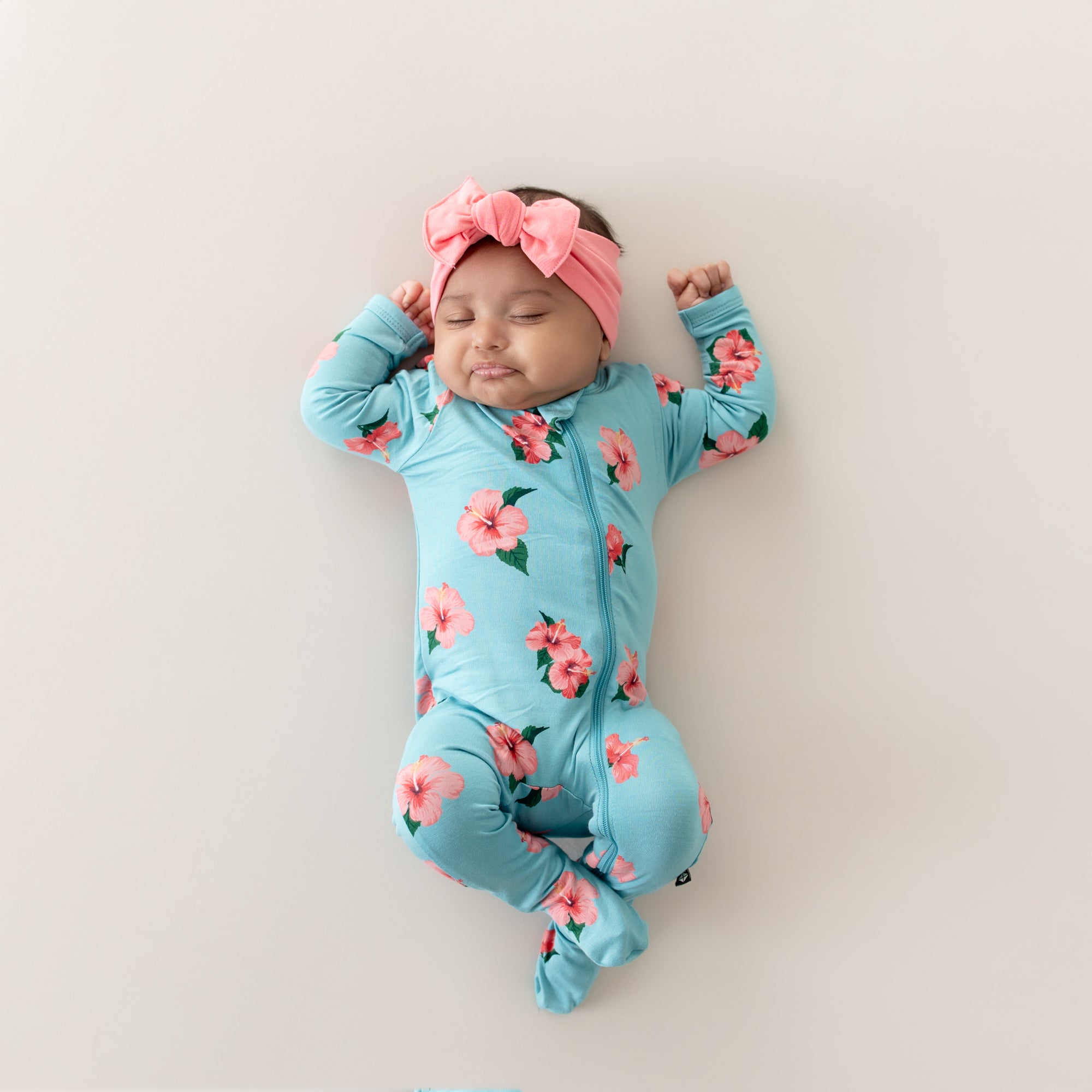 Baby sleeping wearing Kyte Baby Zippered Footie in Hibiscus