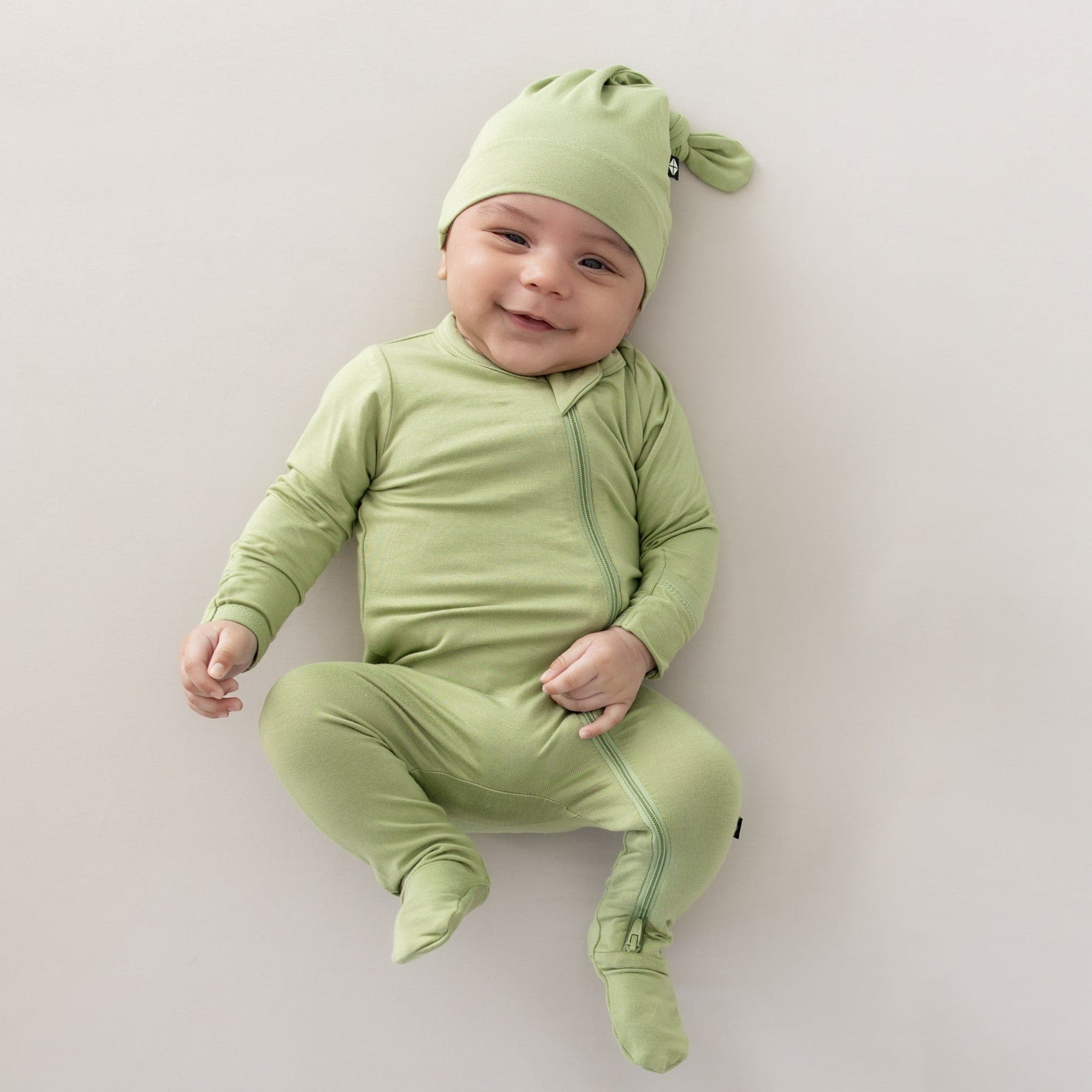 baby smiling wearing honu zippered footie and knotted cap