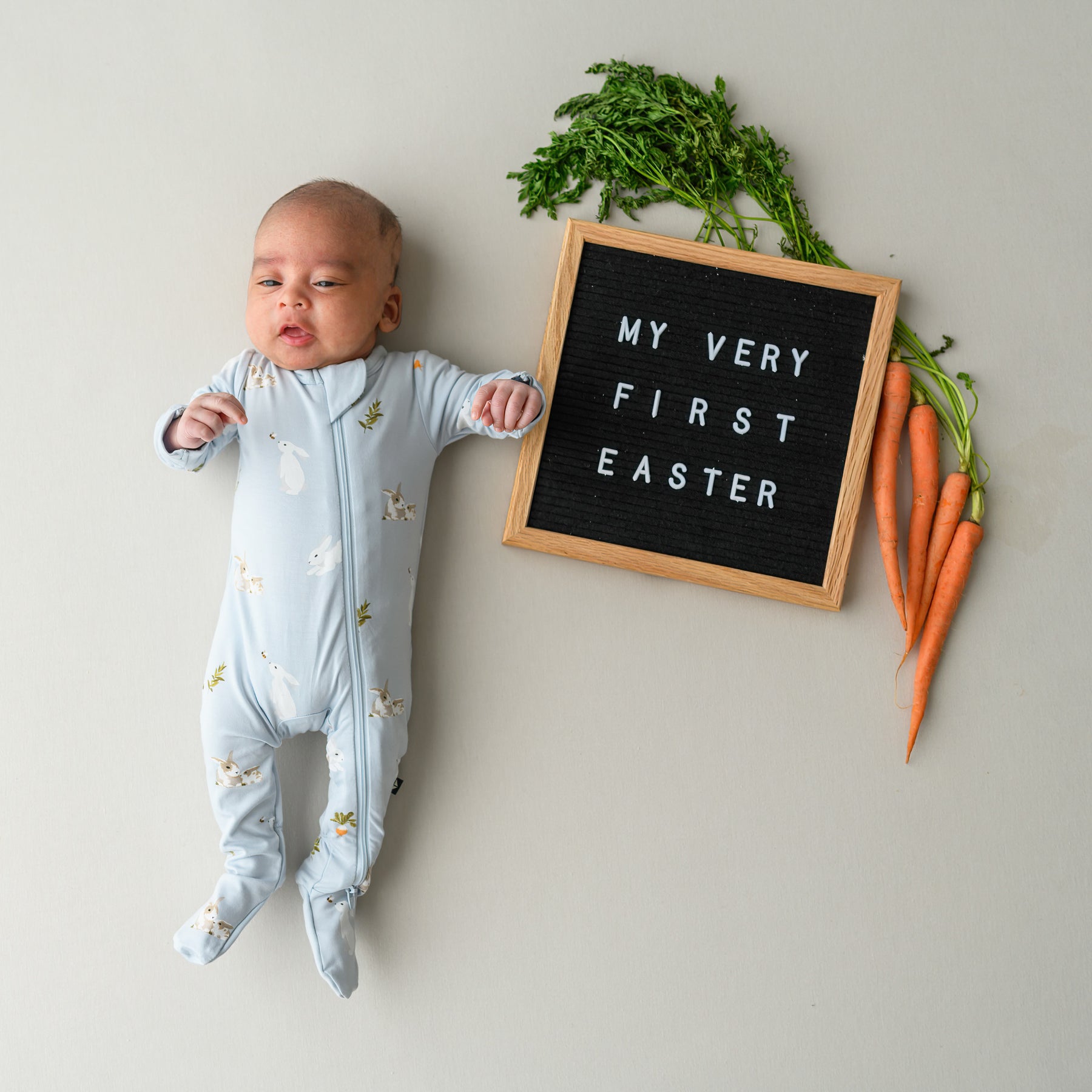 baby in Zippered Footie in Ice Rabbit next to first easter sign