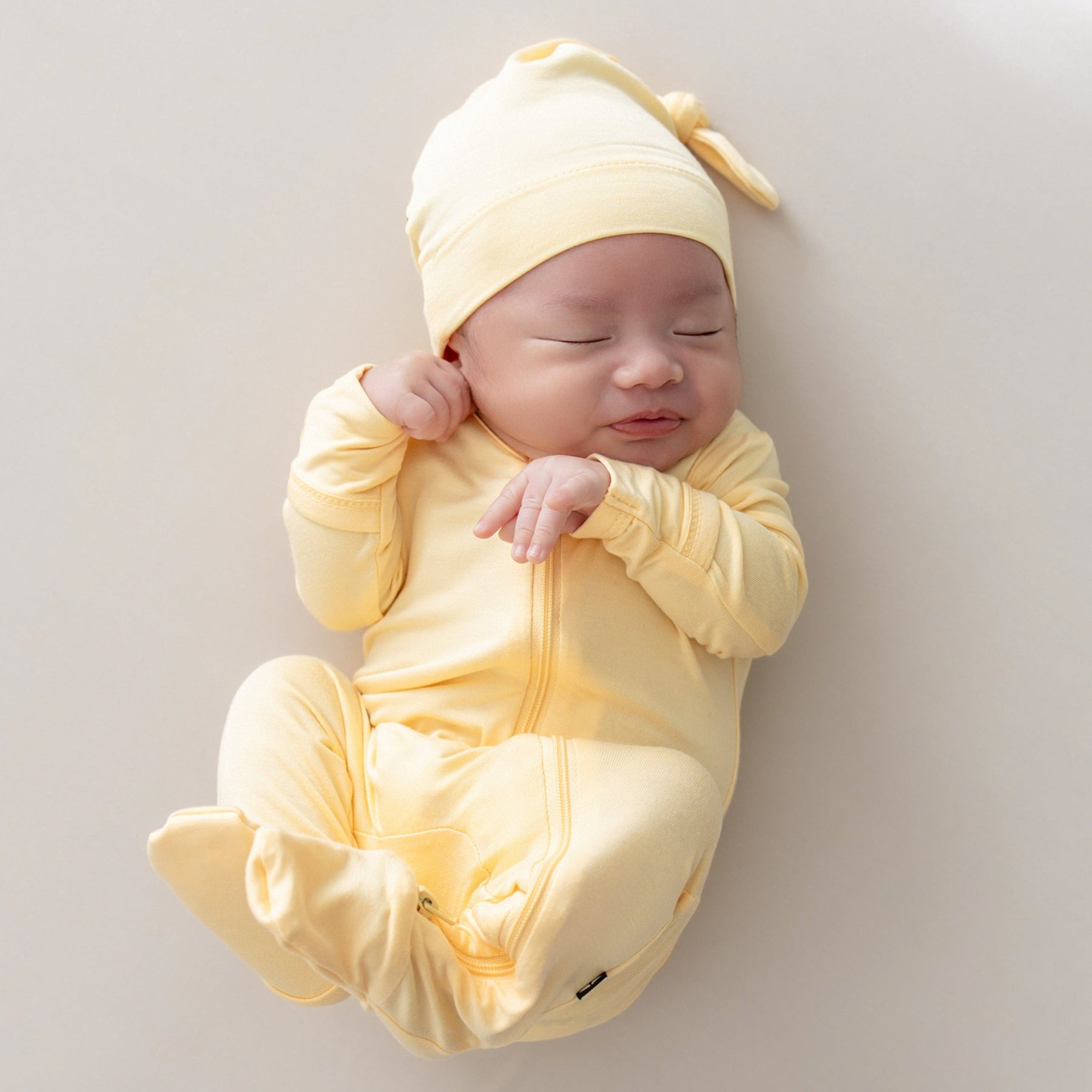 baby snuggled up in a zippered footie and knotted cap in lilikoi