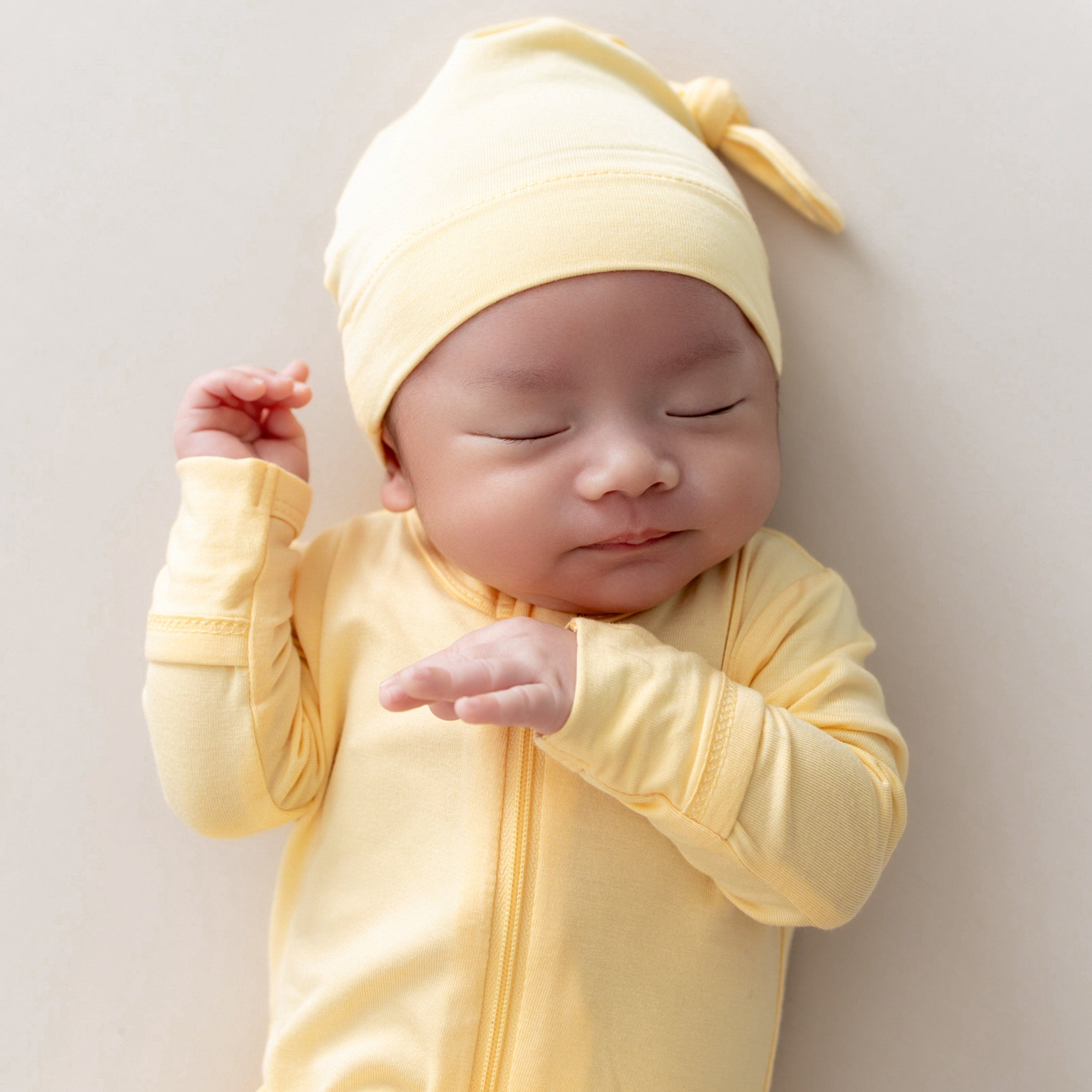 sleeping baby wearing knotted cap and zippered footie in lilikoi close up shot 