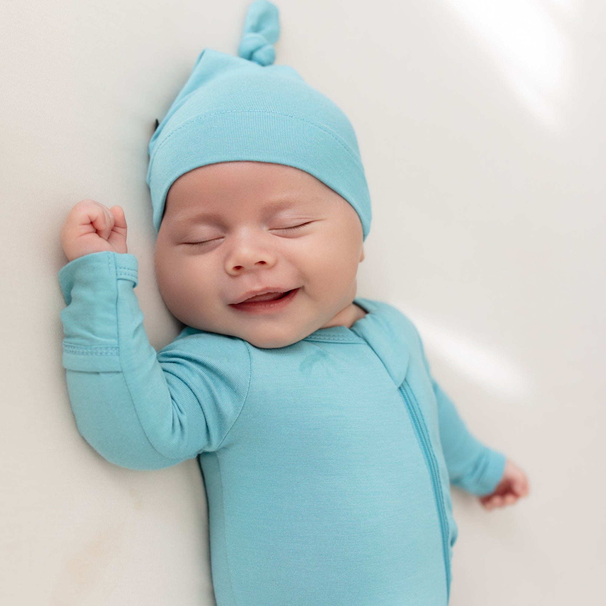 close up of baby sleeping and smiling while wearing zippered footie and knotted cap in makai