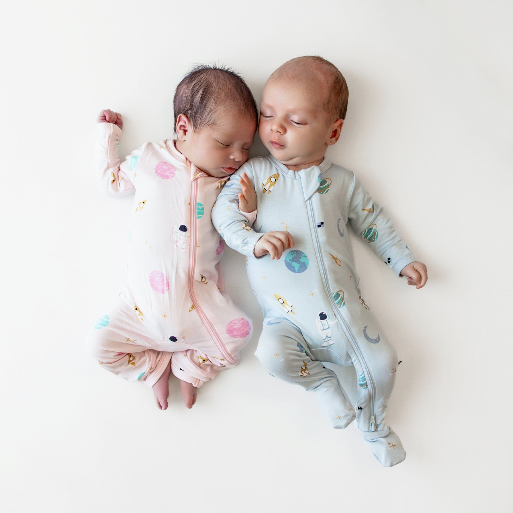 two babies sleeping wearing a zippered romper in sakura space and zippered footie in ice space