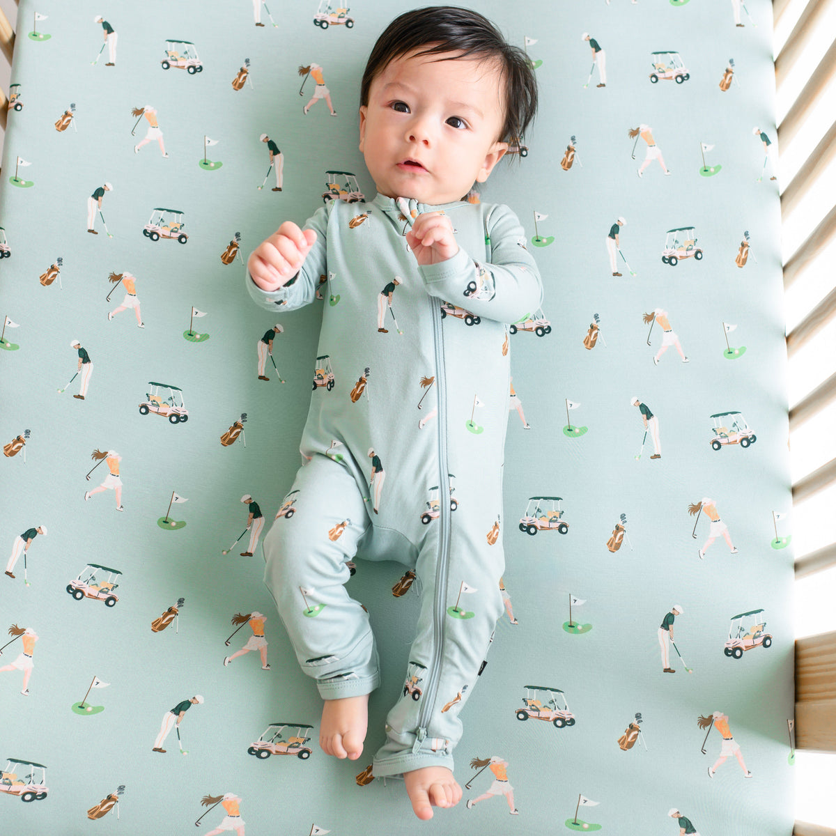 Baby in Zippered Romper laying on crib with Crib Sheet in Golf 