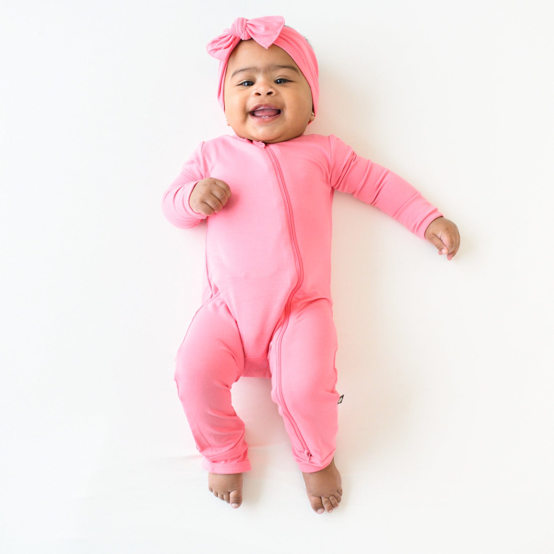 baby wearing zippered romper in guava with matching bow 