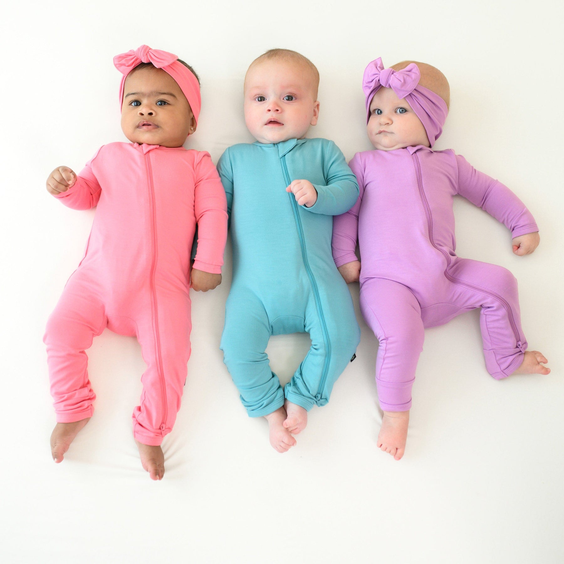 3 babies wearing zippered rompers in guava, makai and poi