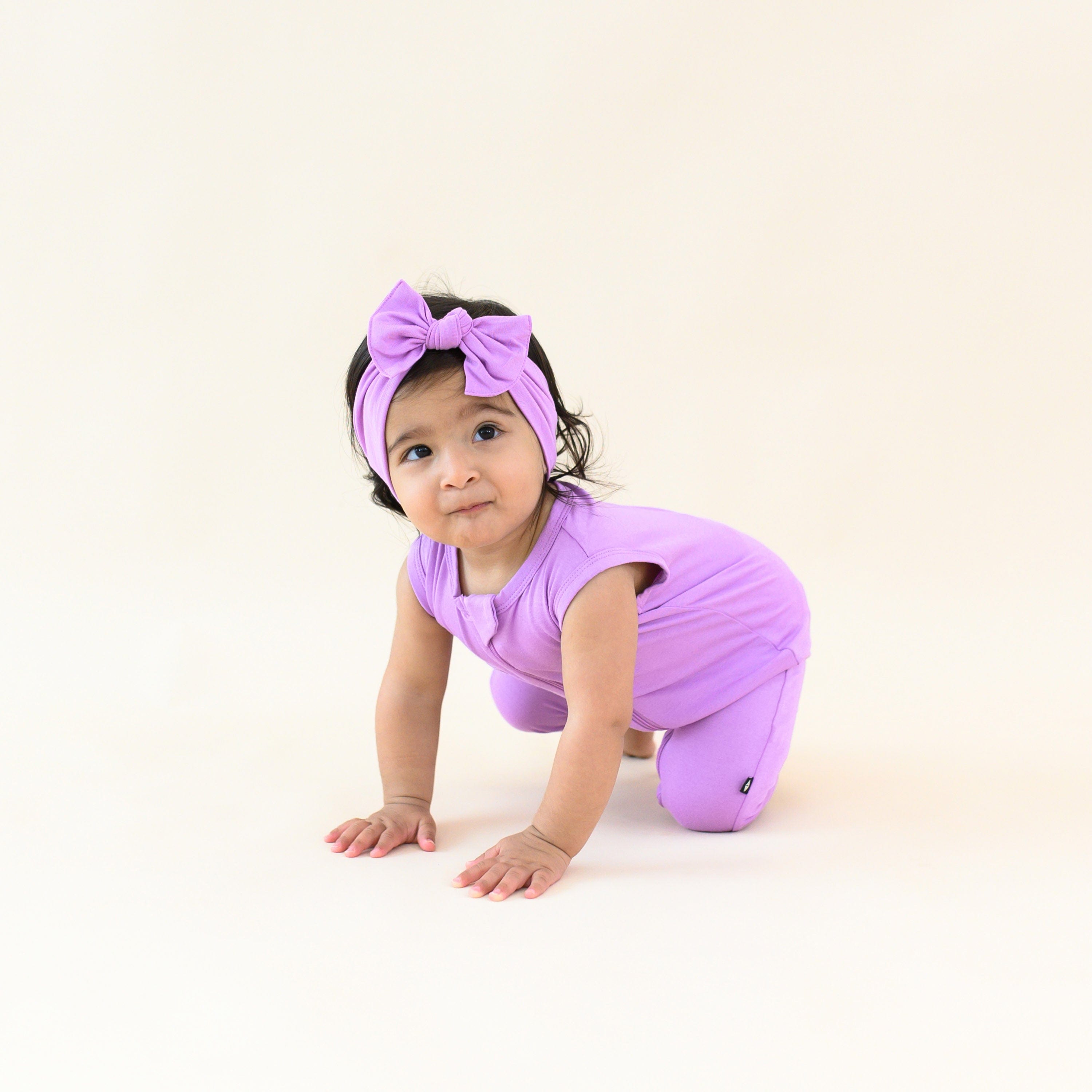 baby crawling wearing sleeveless zippered romper and bow in poi