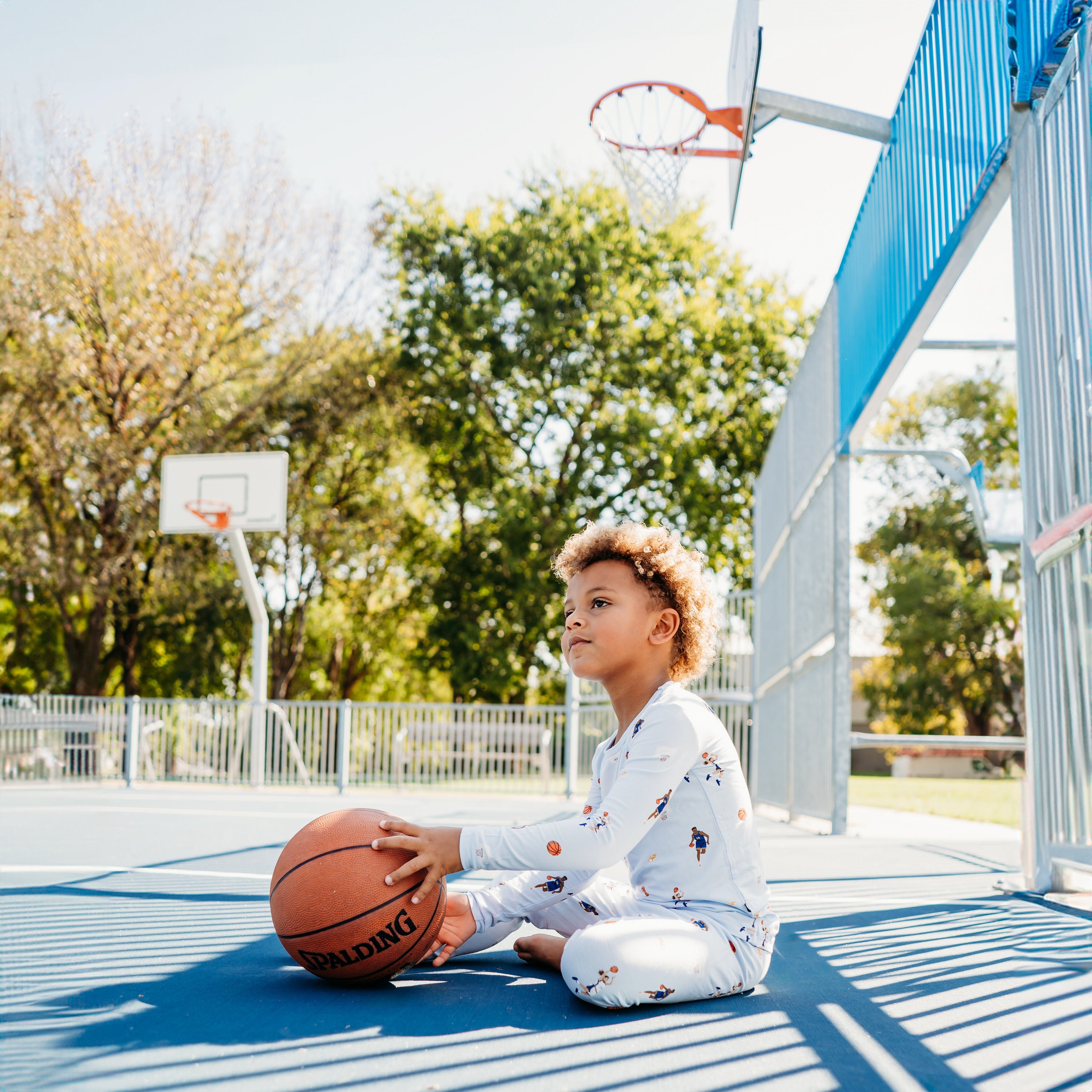 Boy sitting on a basketball court with a basketball wearing the Long Sleeve Pajamas in Basketball