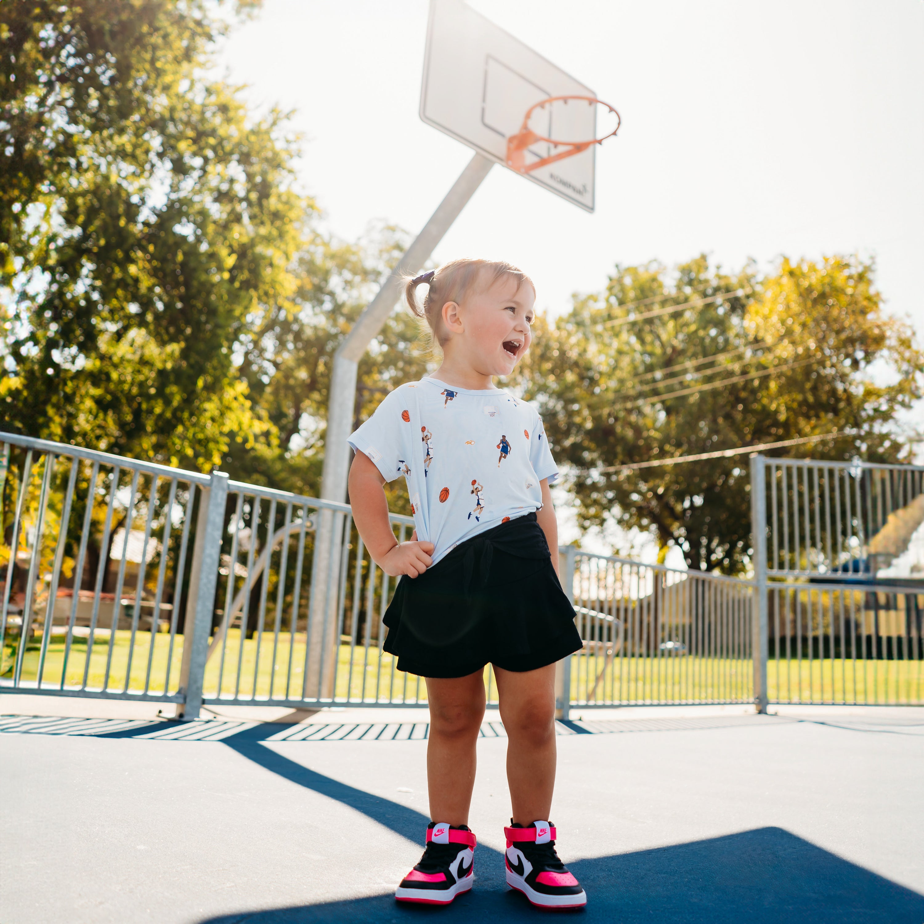 Young girl wearing the Toddler Basic Tee in Basketball and black skirt standing on a basketball court