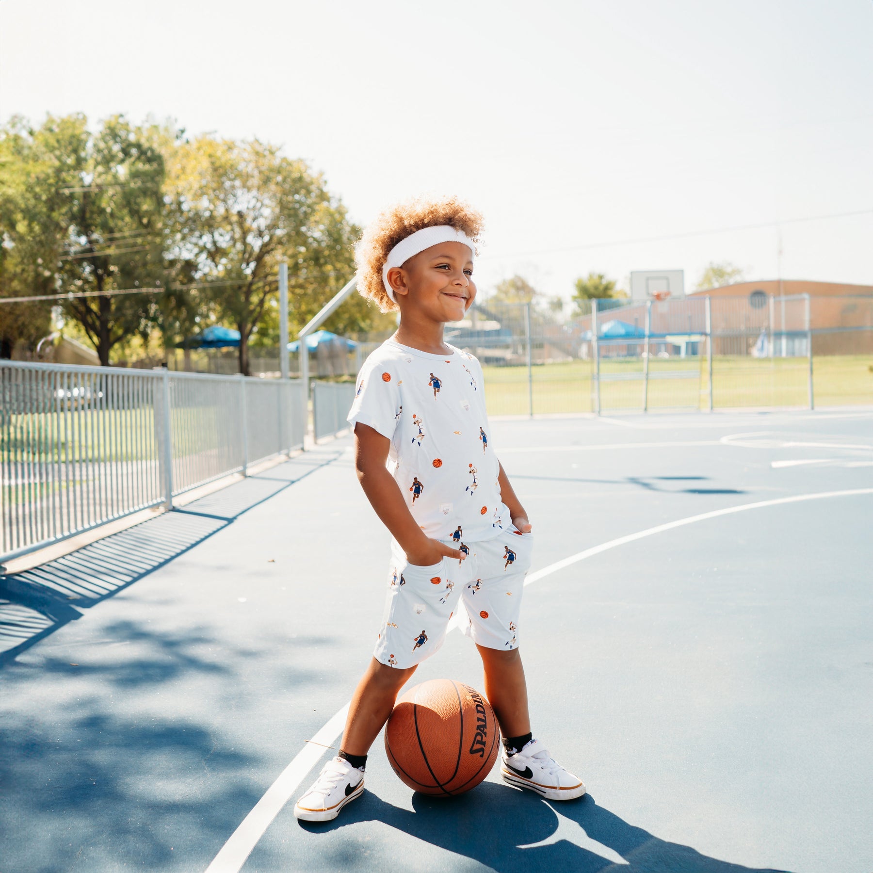Young boy standing on a basketball court with his hands in the pockets of the Drawstring Short in Basketball wearing a matching basic tee