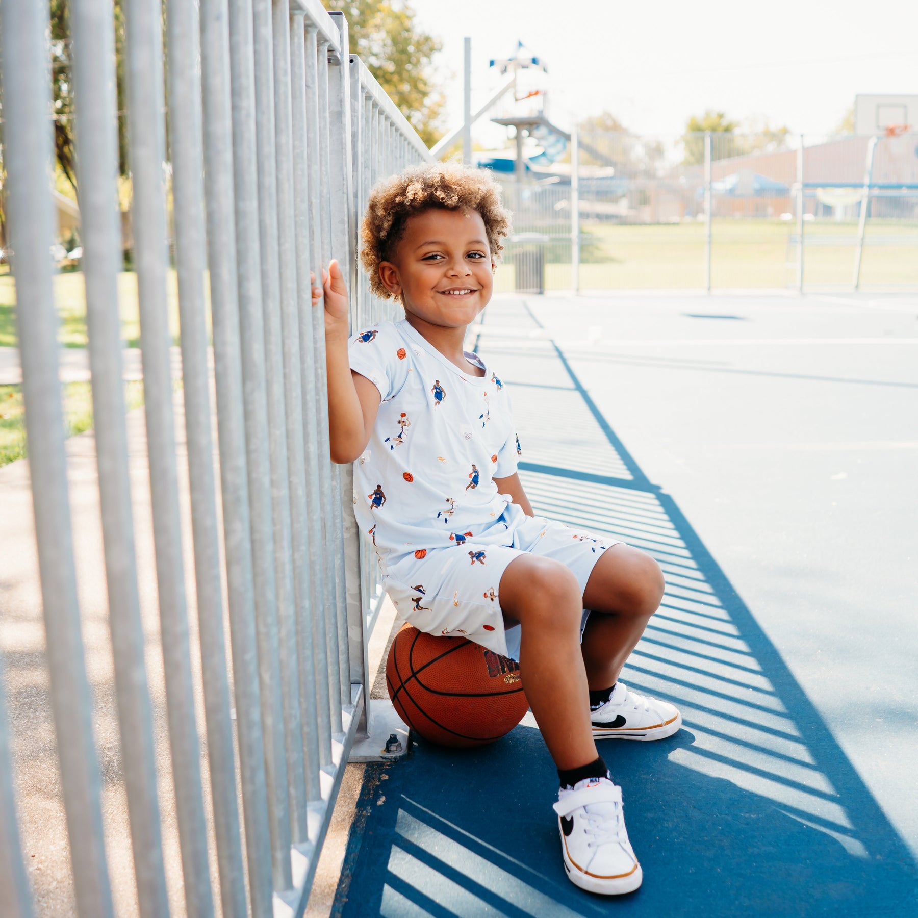 Young boy sitting on a basketball on a basketball court wearing the Drawstring Short in Basketball with matching basic tee