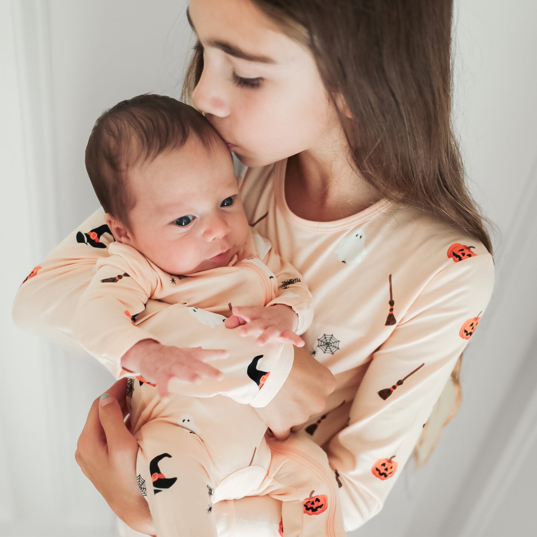 Infant wearing the Zippered Footie in Bewitched being held and kissed by big sister who is matching in long sleeve toddler pajamas