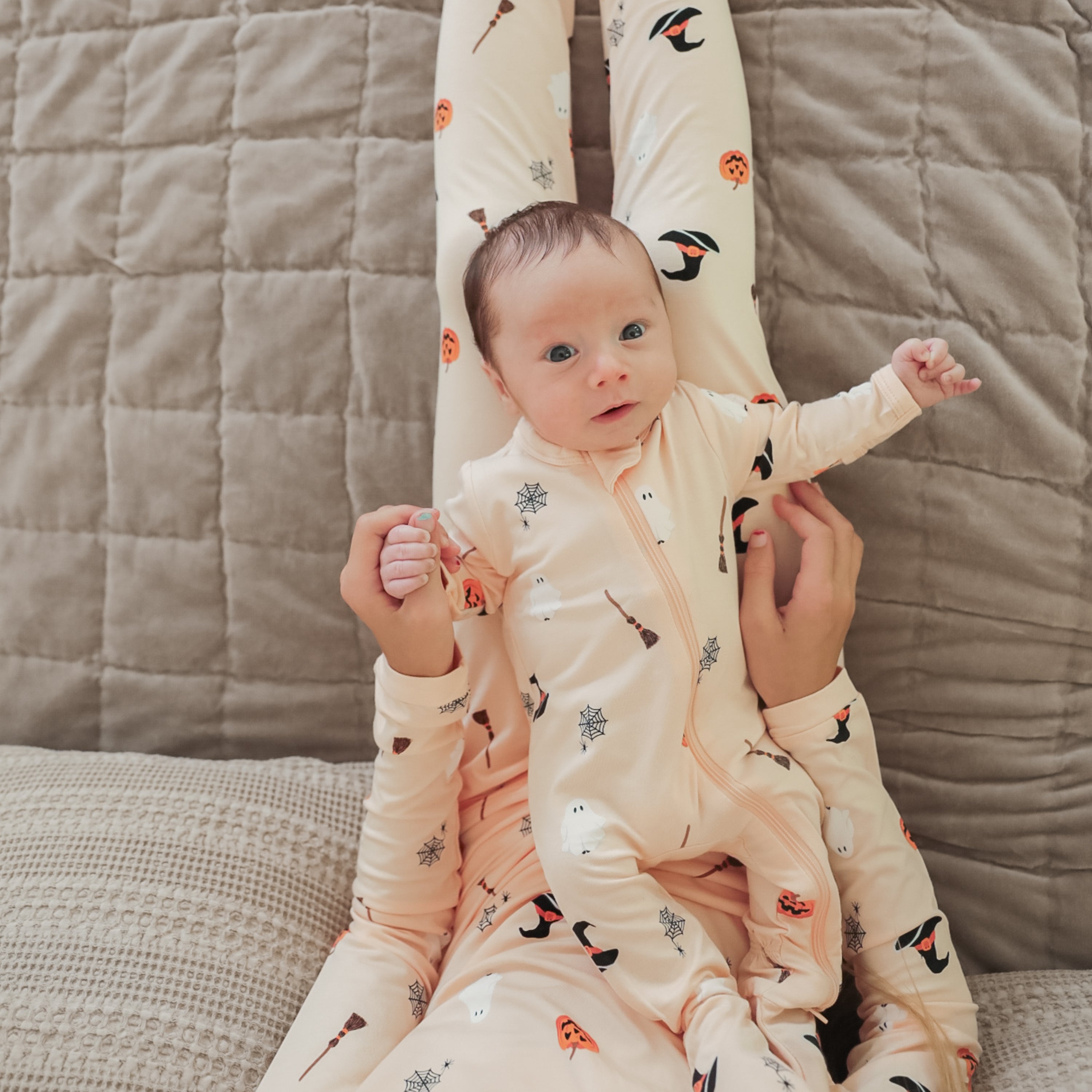 Infant wearing the Zippered Footie in Bewitched laying down on the legs of big sister who is wearing matching long sleeve pajamas